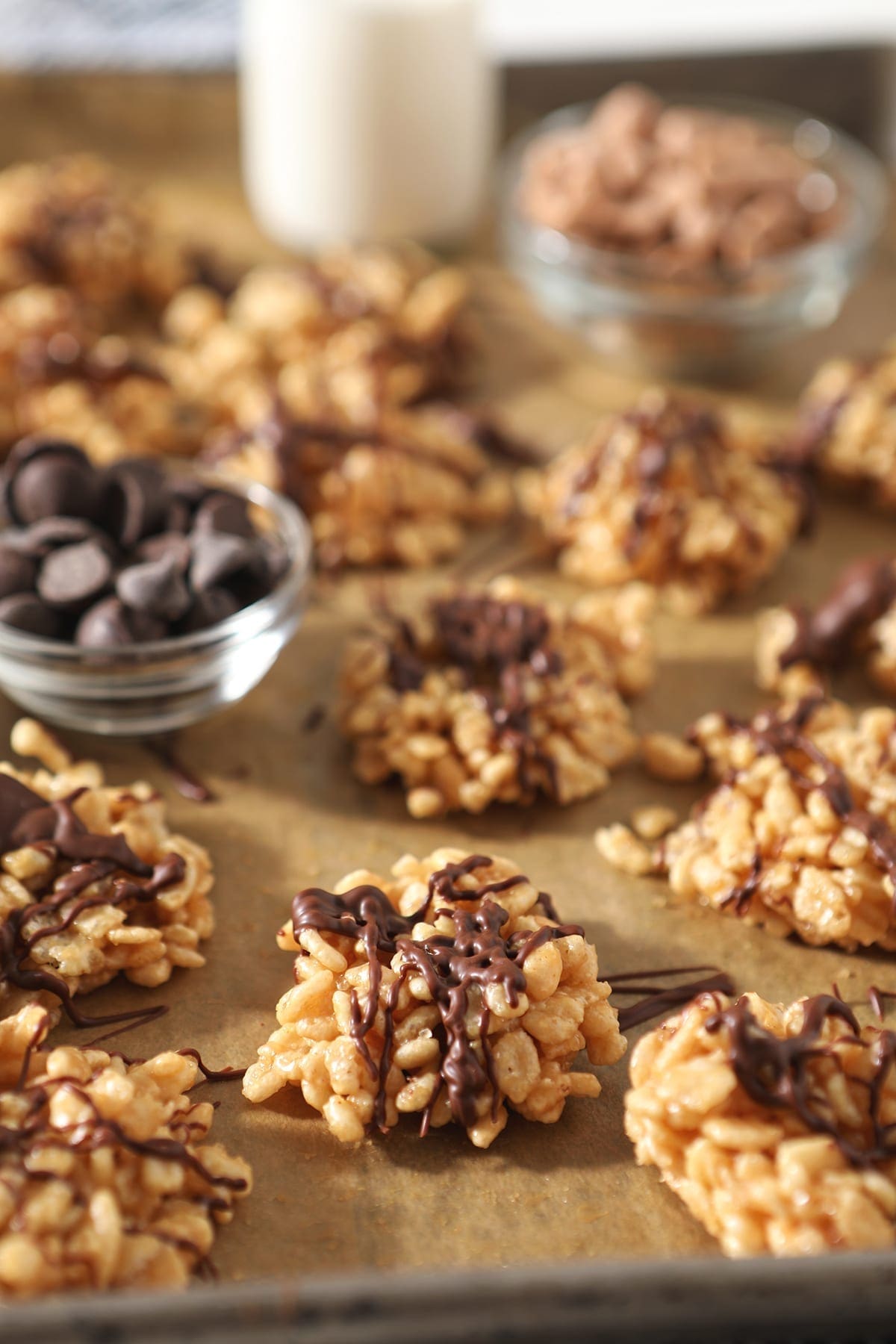 Several Chocolate Peanut Butter No Bake Cookies sit on a baking sheet lined in parchment with bowls of chocolate chips and butterscotch chips