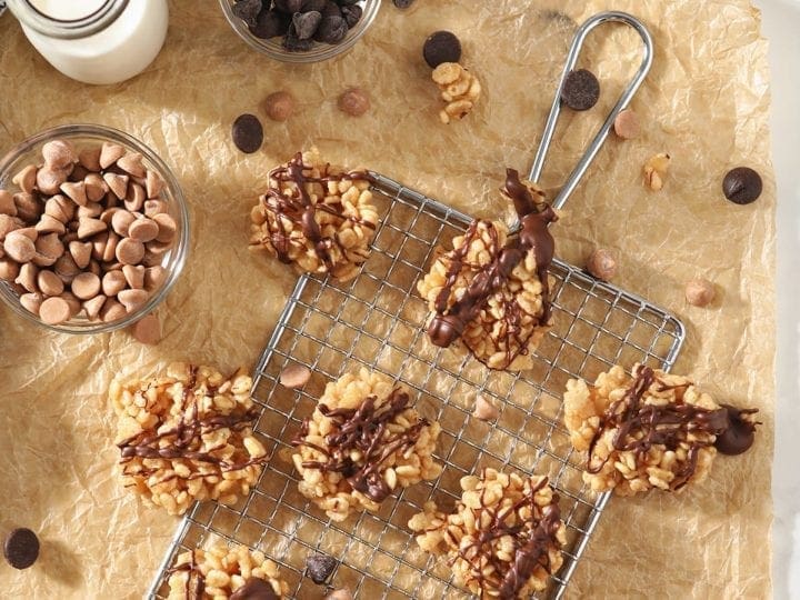 Several Chocolate Peanut Butter No Bake Cookies sit on a silver grate and brown parchment paper, surrounded by ingredients and a bottle of milk
