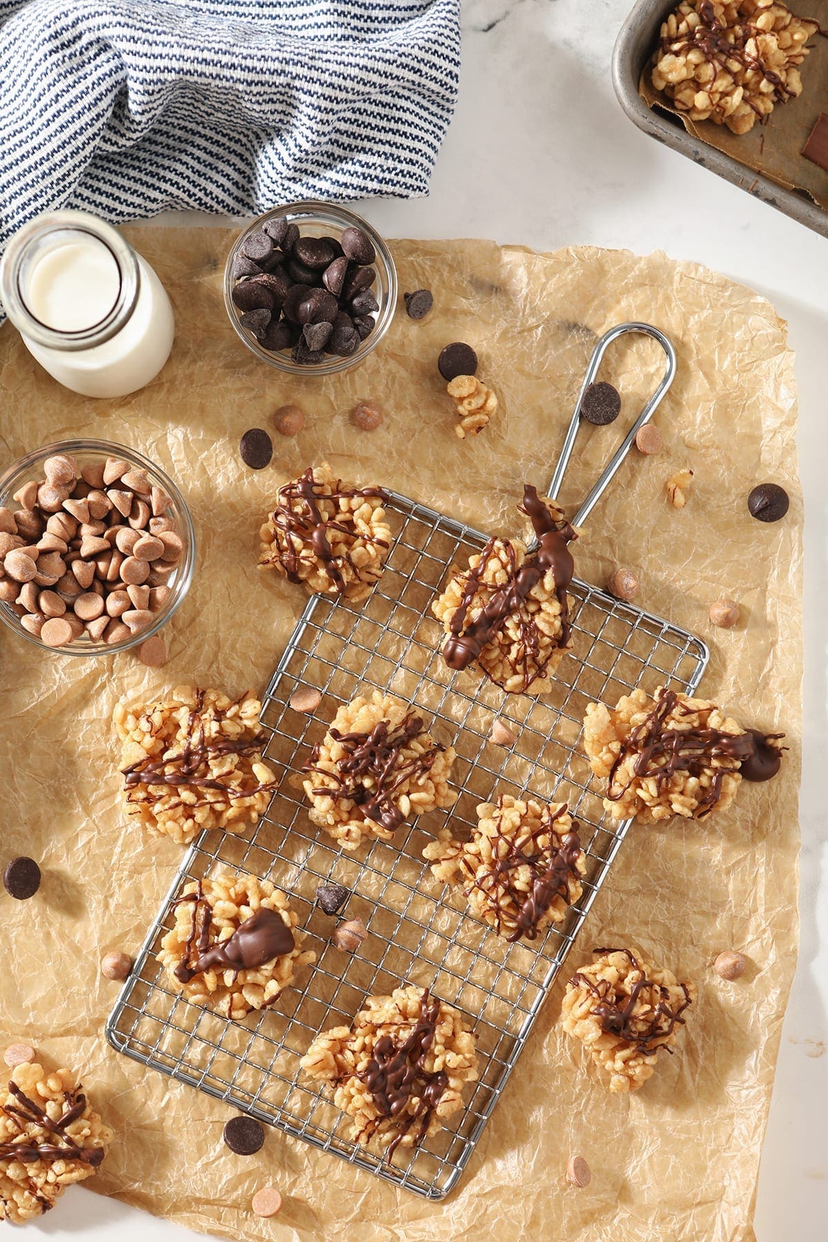 Several Chocolate Peanut Butter No Bake Cookies sit on a silver grate and brown parchment paper, surrounded by ingredients and a bottle of milk