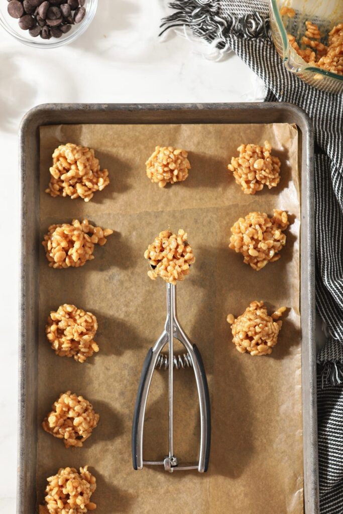 A cookie scoop holds a no bake cookie on a baking sheet with others