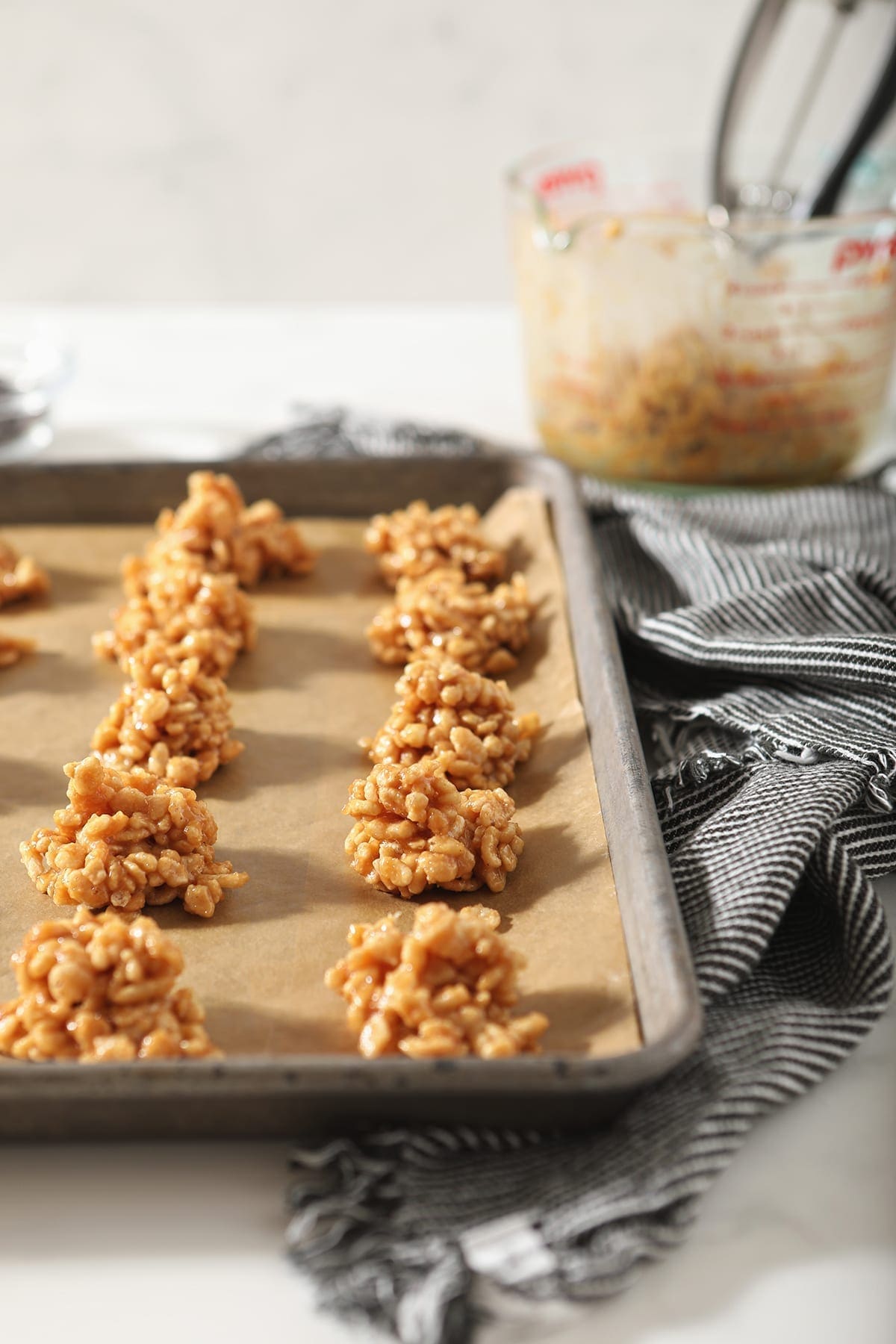 A lined baking sheet holds no bake peanut butter cookies on a marble surface with a grey and white towel