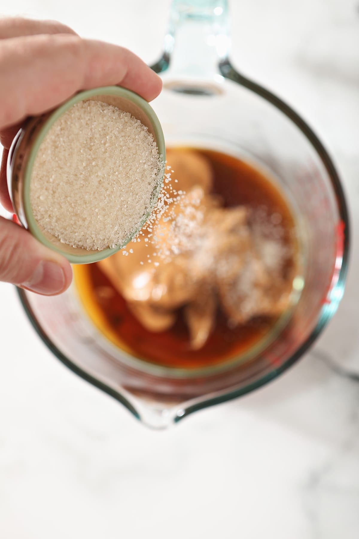 Sugar sprinkles into a measuring cup on top of peanut butter and maple syrup, from above