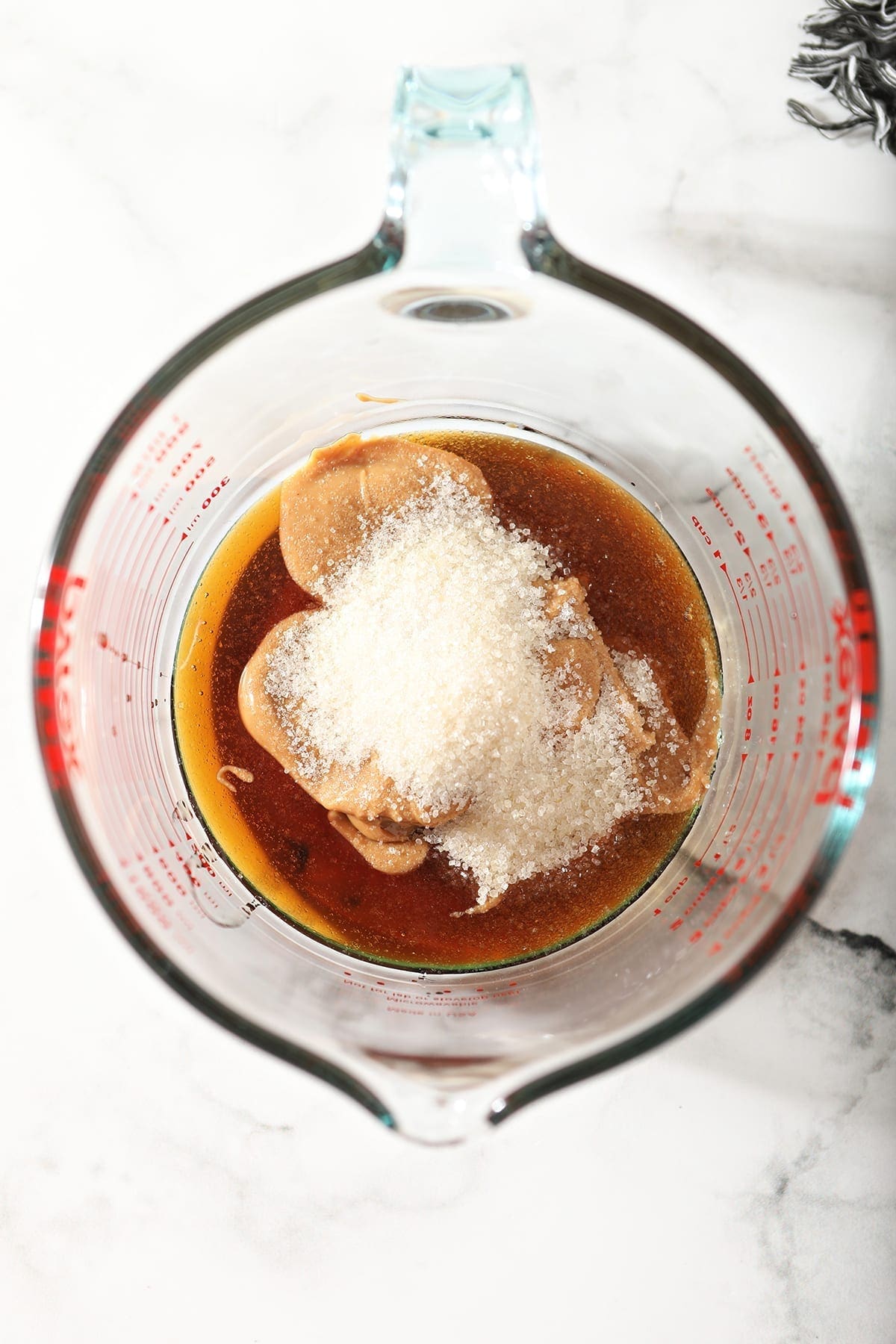 Maple syrup, peanut butter and sugar in a glass measuring cup on a marble counter