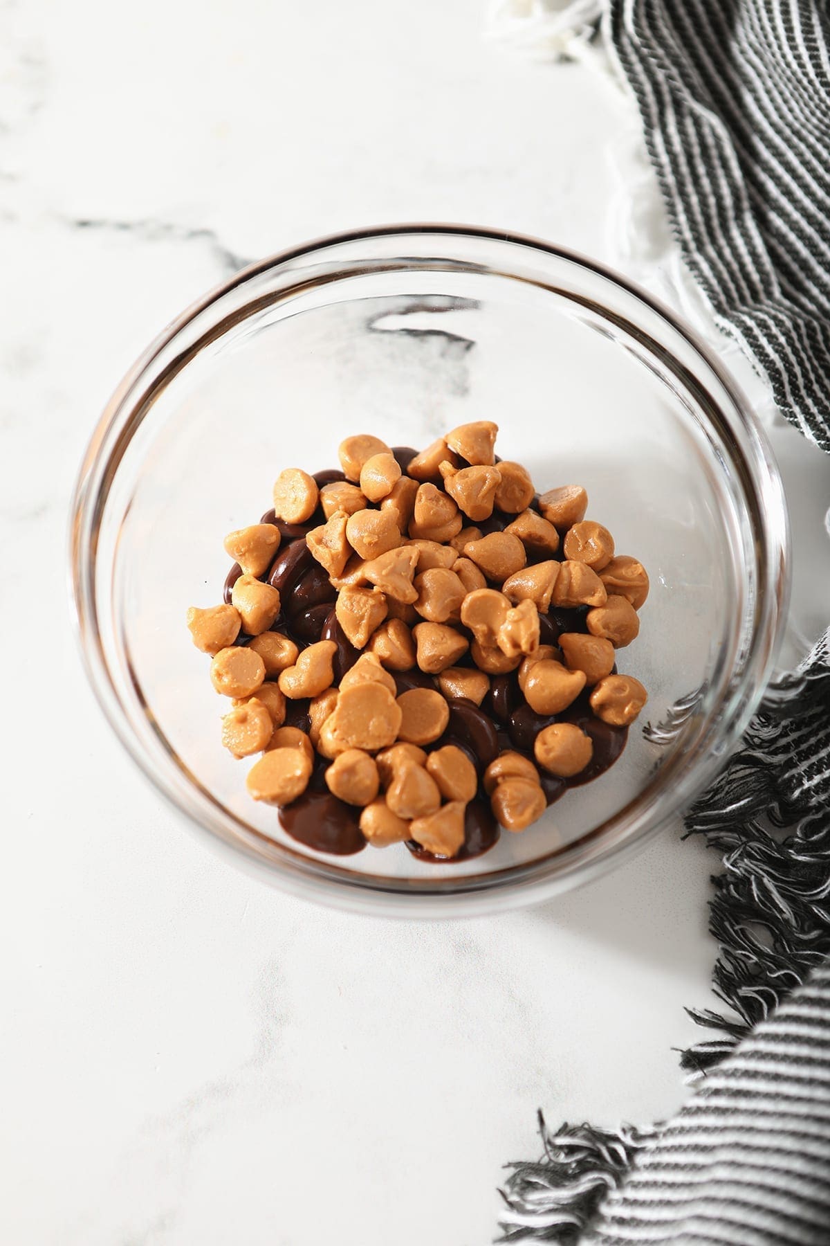 Butterscotch and chocolate chips in a clear glass container on marble