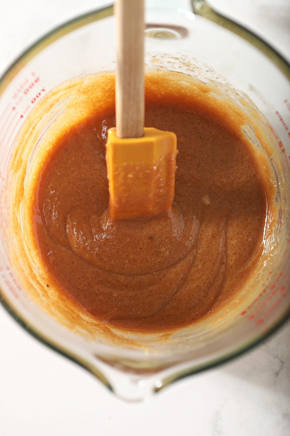 Wet ingredients in a liquid measuring cup with a yellow rubber spatula