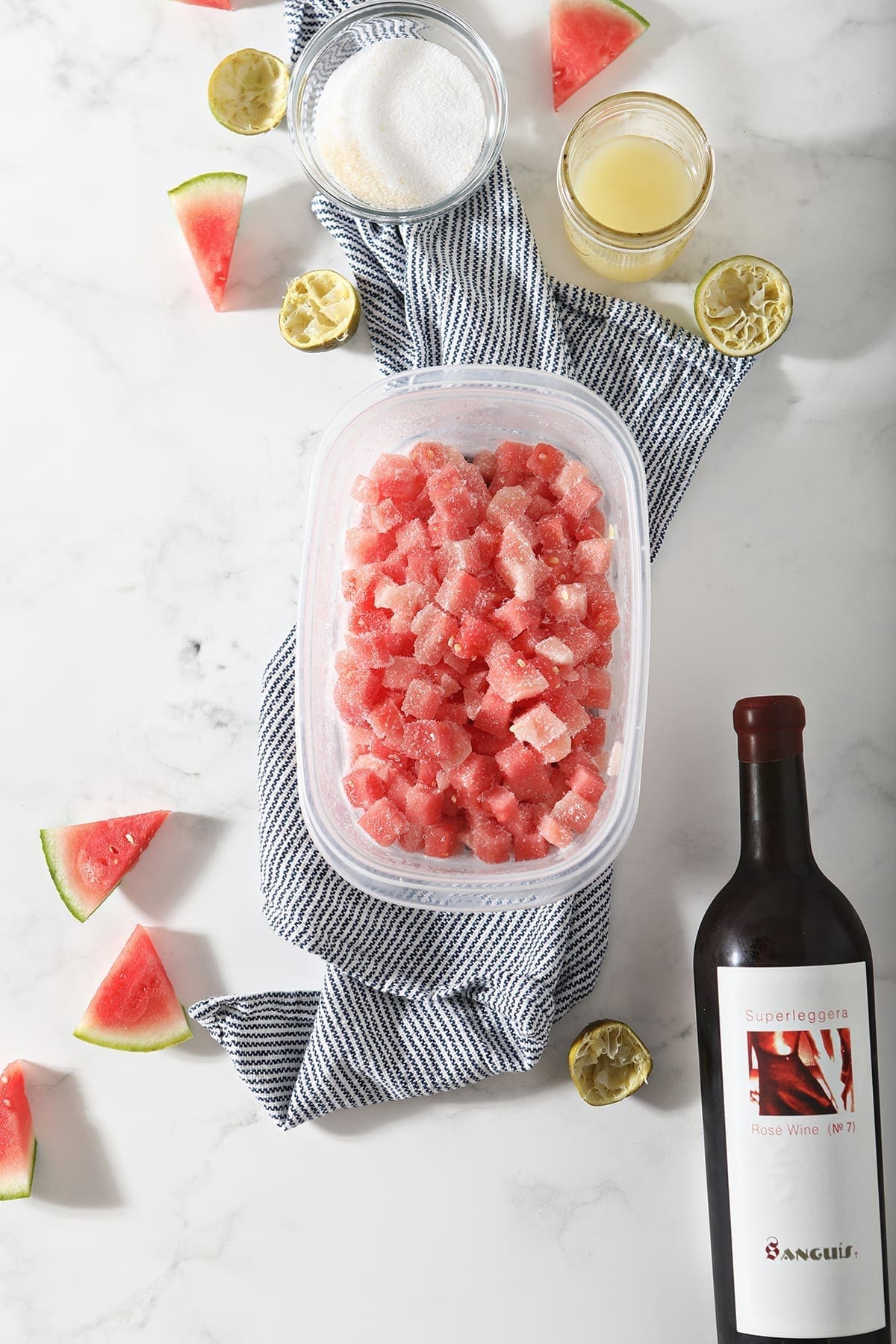 Frozen watermelon, rose wine, lime juice and sugar on a blue striped towel on marble