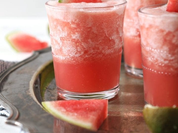 Three glasses holding pink slushy Watermelon Froses garnished with watermelon wedges on a silver platter