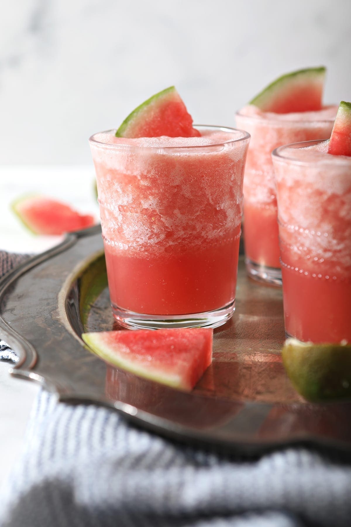 Three glasses holding pink slushy Watermelon Froses garnished with watermelon wedges on a silver platter