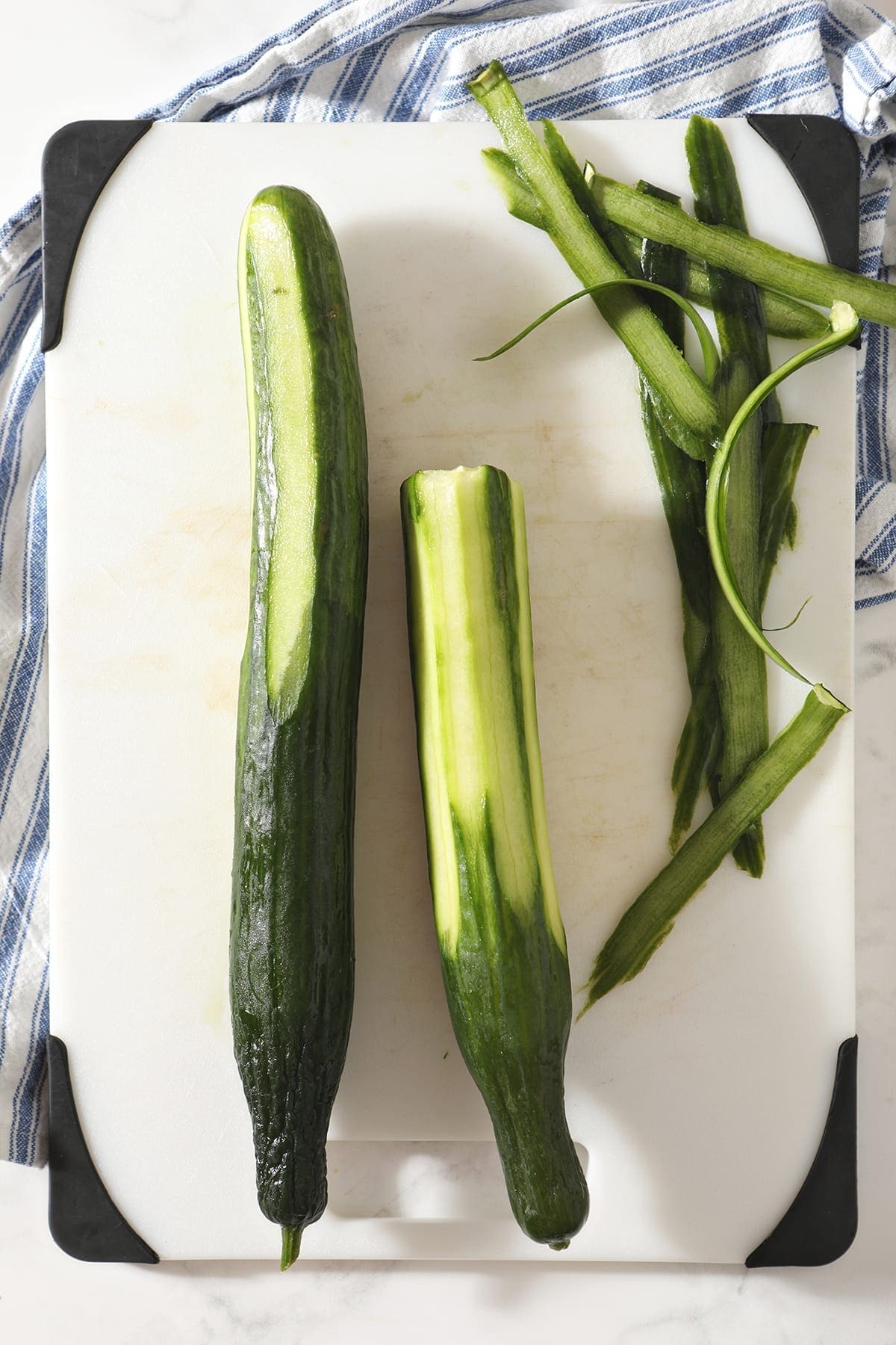 Two half-peeled English cucumbers on a white cutting board