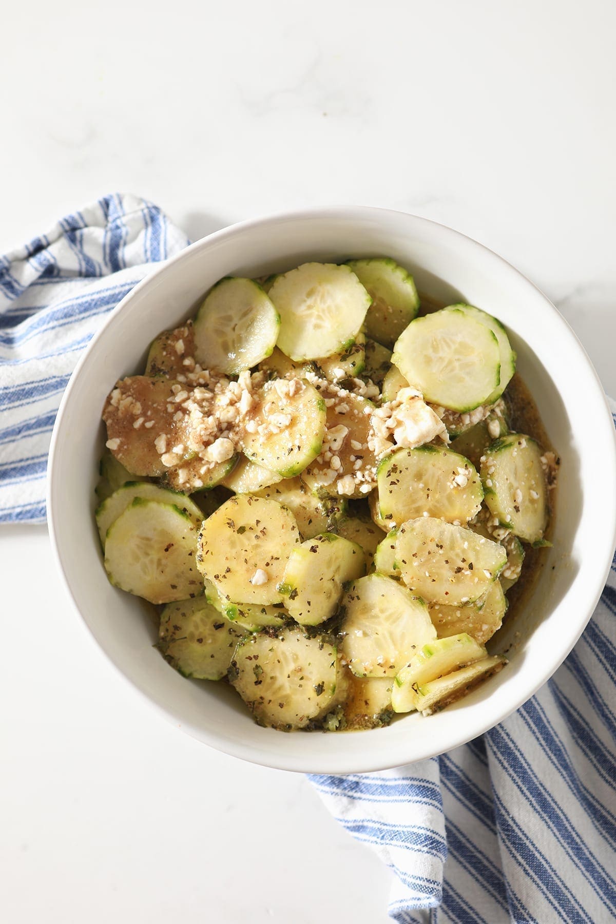 Easy Cucumber Salad with Feta Vinaigrette in a white bowl on top of a blue and white striped towel