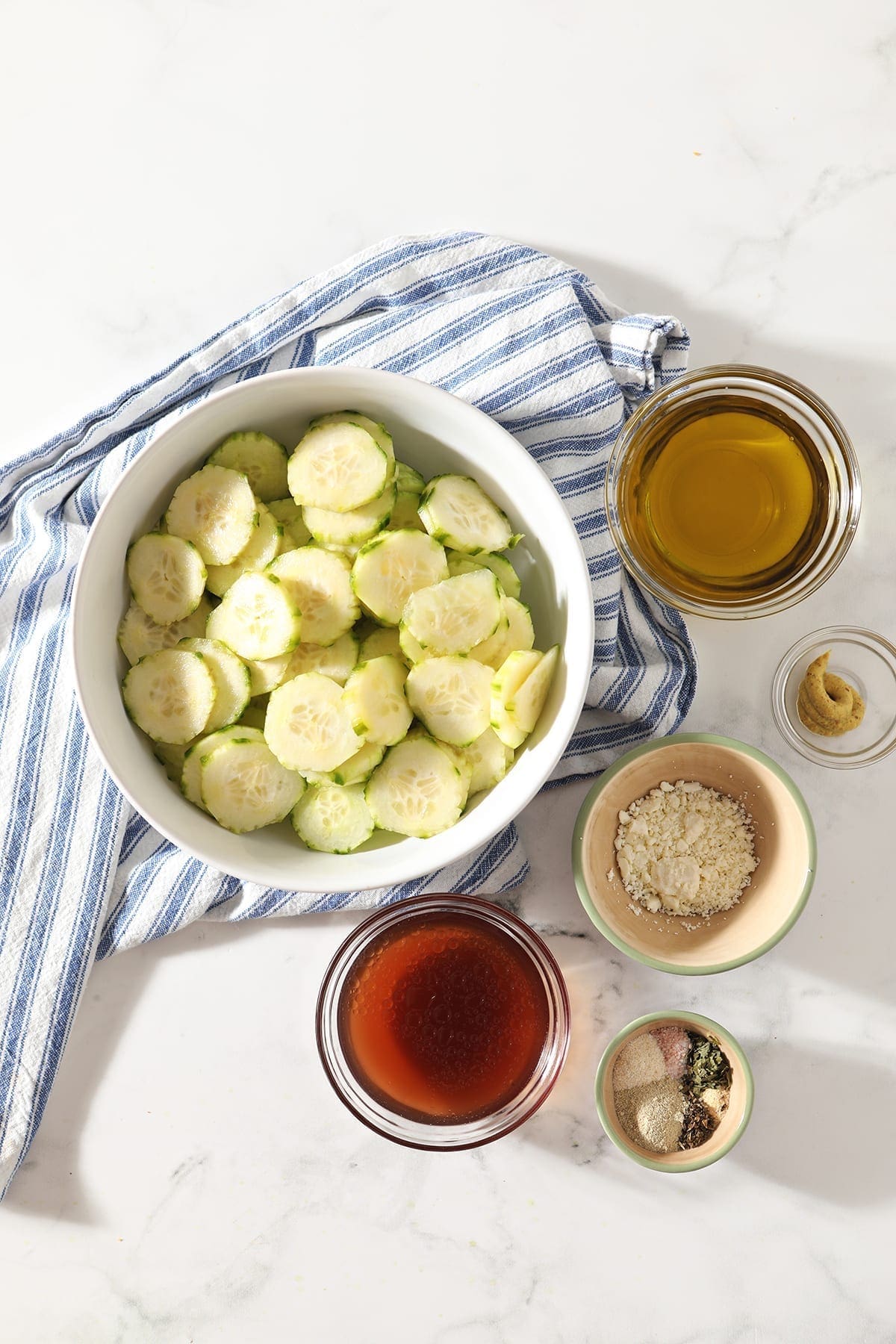 A bowl of cucumber rounds with other ingredients on a blue and white striped towel