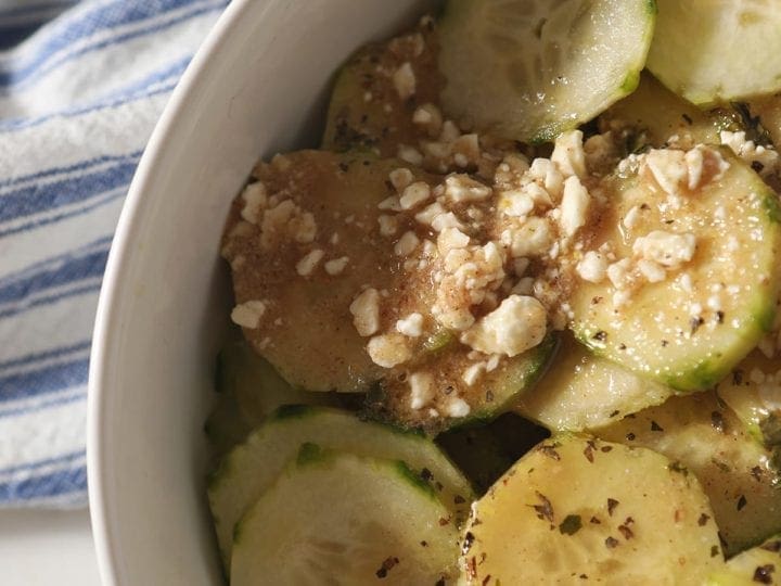 Close up of cucumbers and salad dressing in a white bowl on top of a blue striped towel