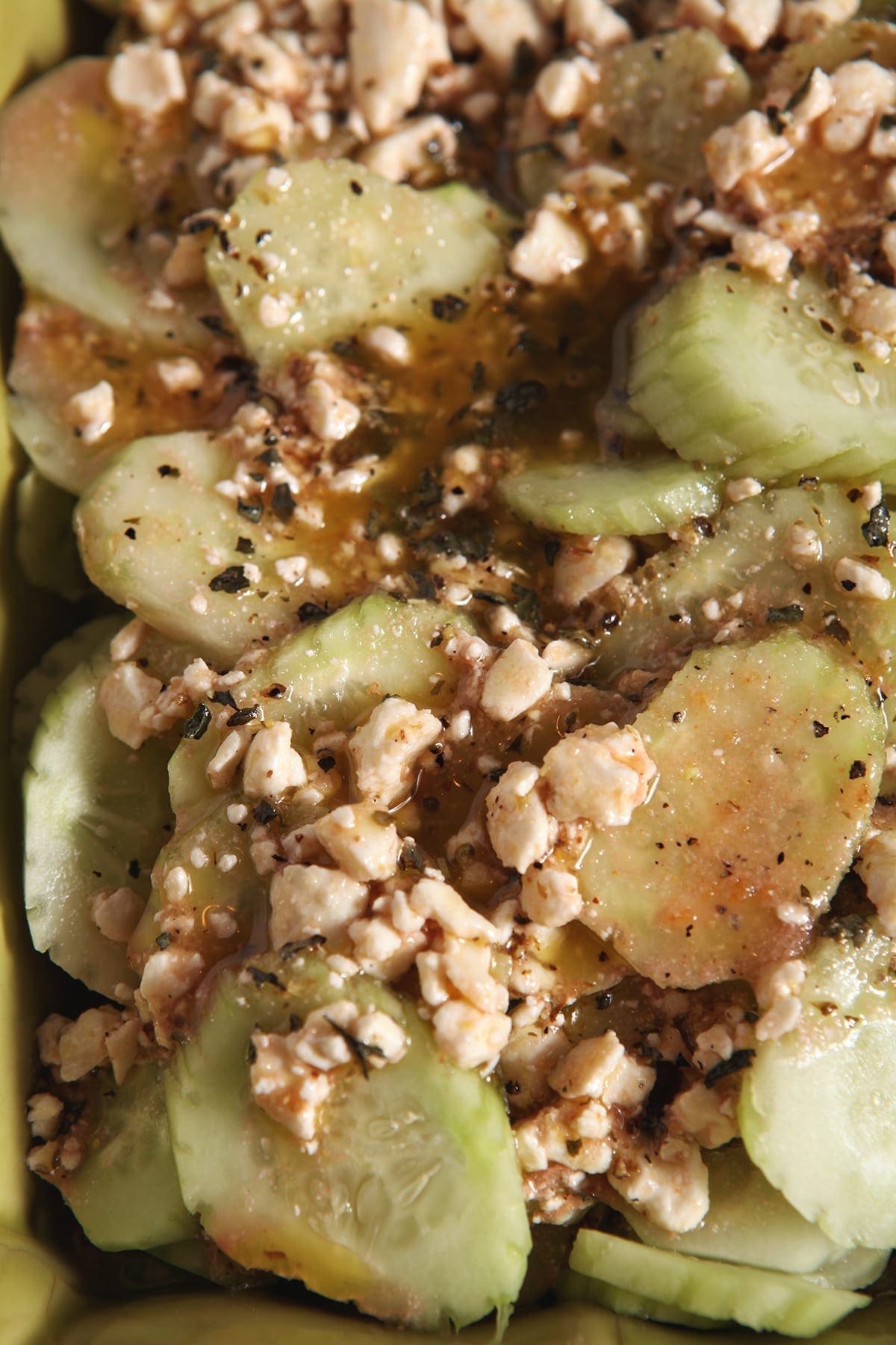 Close up of cucumbers and feta dressing in a green serving dish