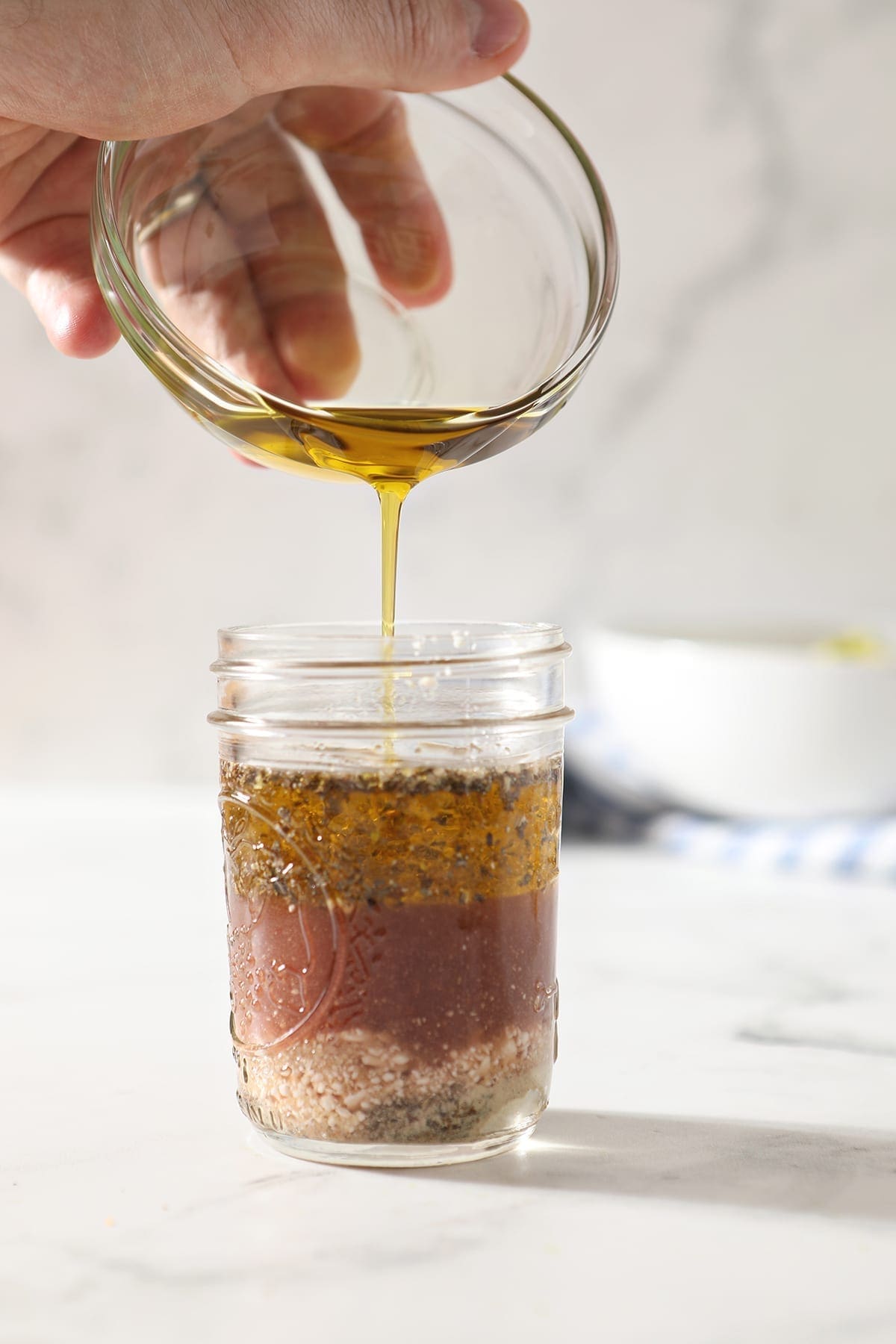 Olive oil drizzles into a mason jar with other feta vinaigrette ingredients