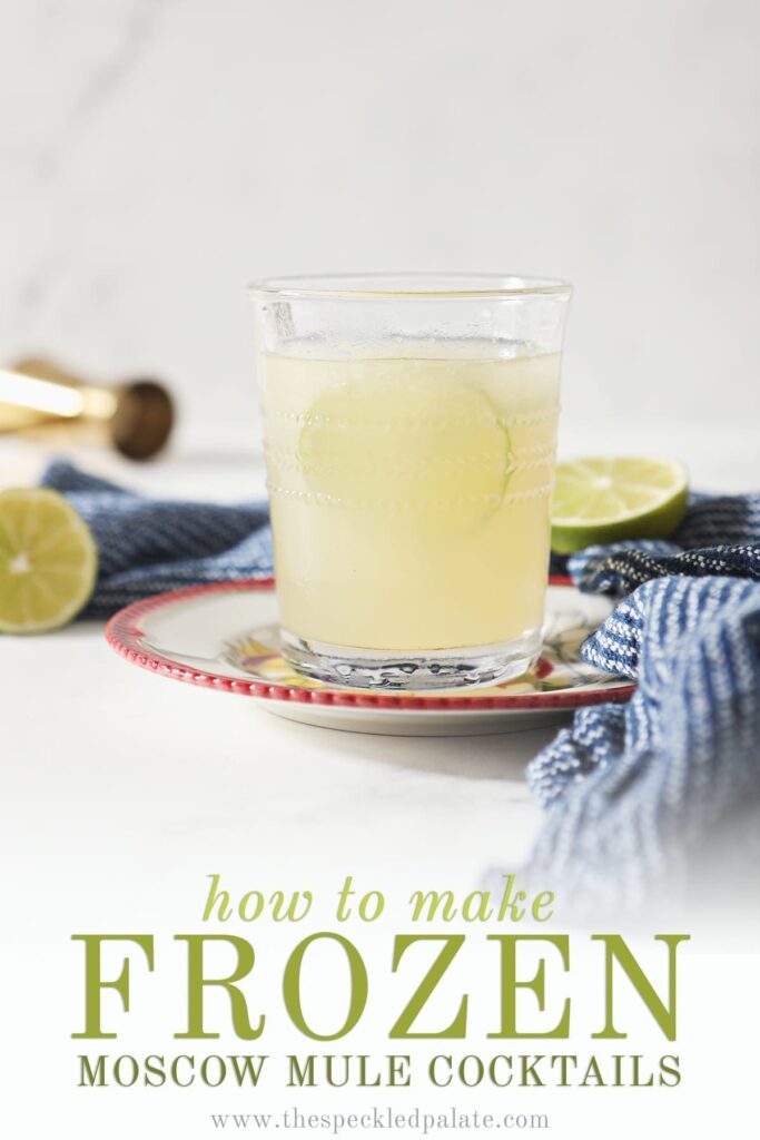 A glass of a Frozen Mule garnished with a lime round sits on a red-rimmed plate by a blue towel on marble with the text "how to make frozen moscow mule cocktails"