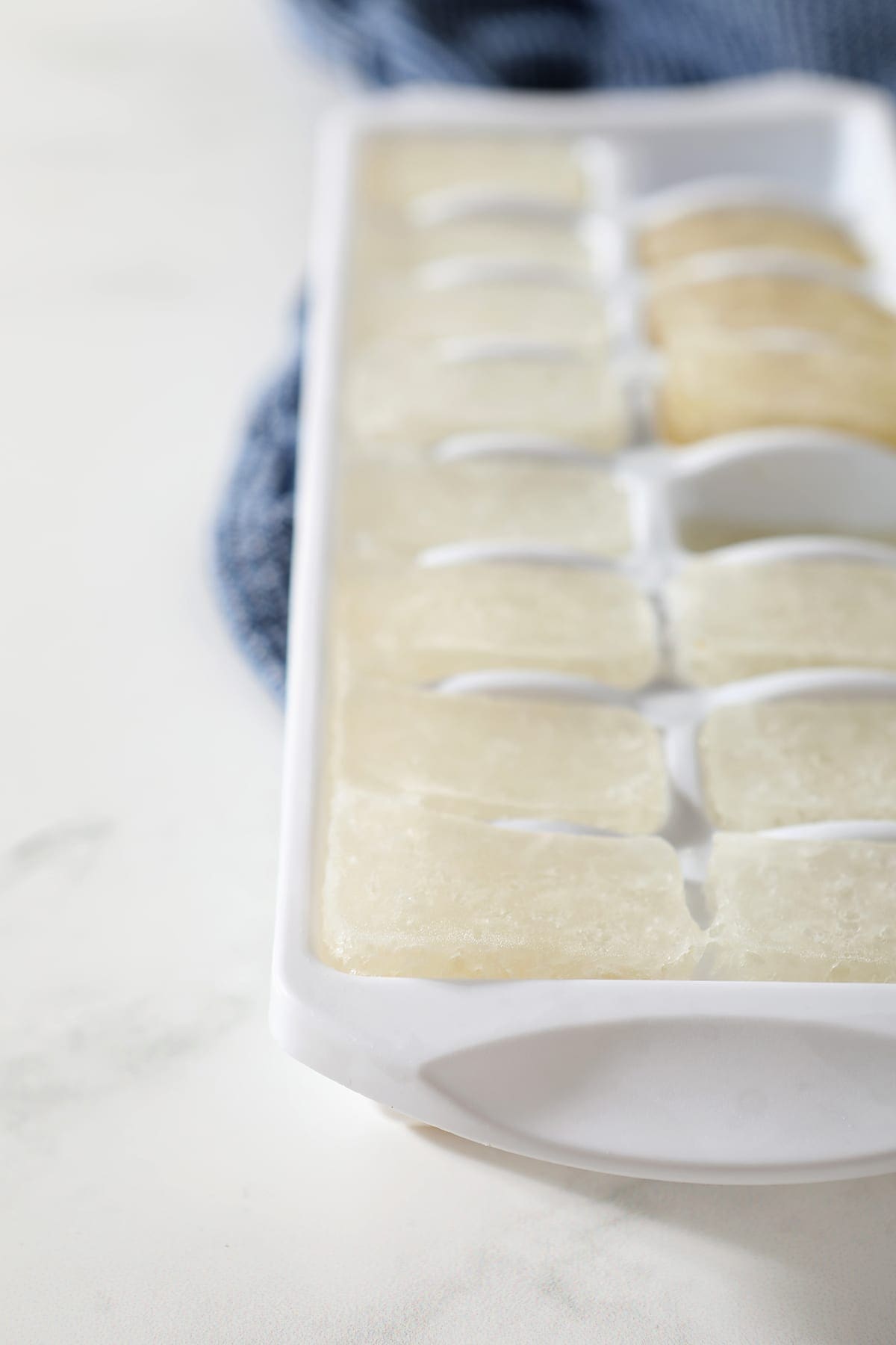 Frozen ginger beer in a white ice cube tray on a marble background with a blue towel