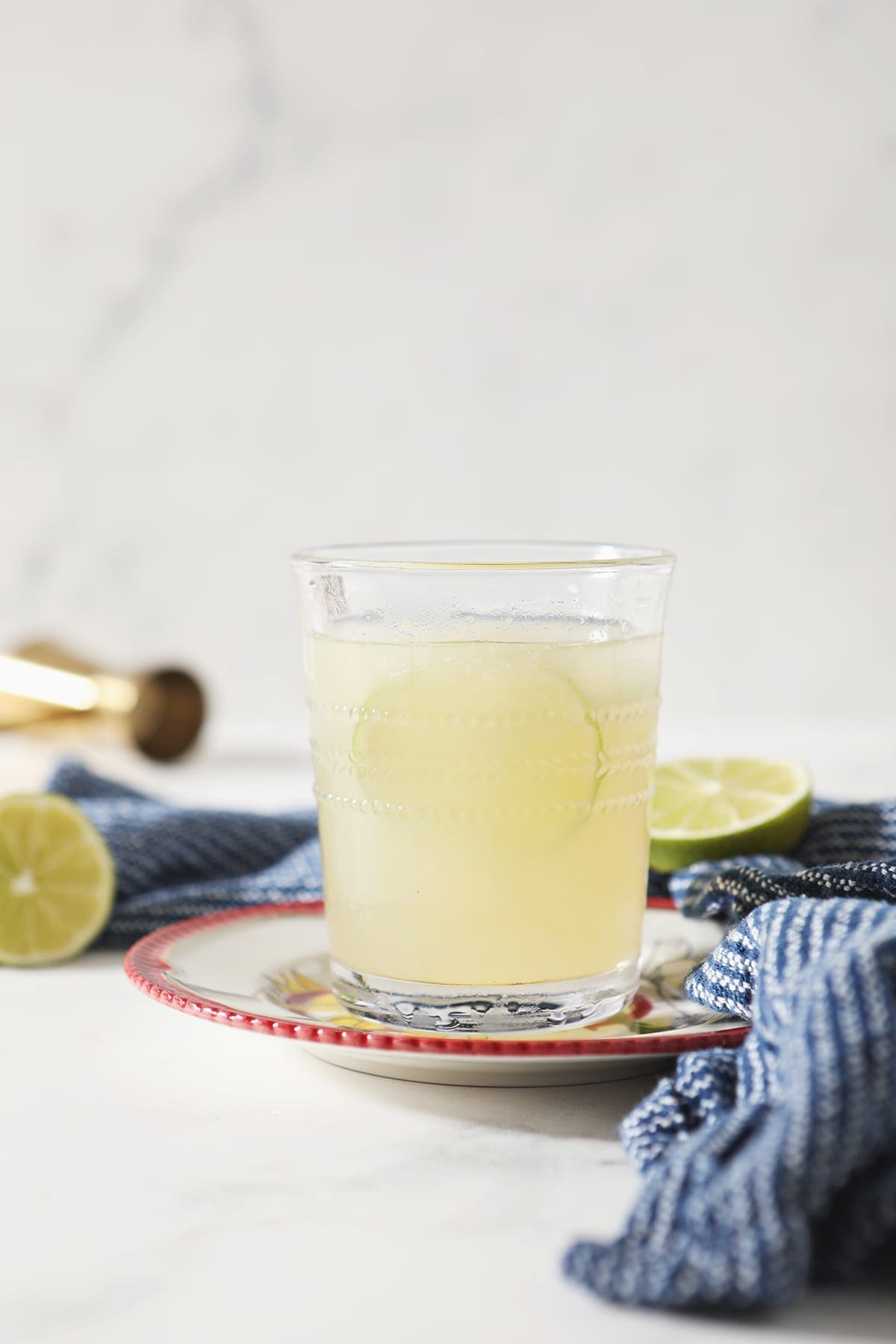 A glass of a Frozen Mule garnished with a lime round sits on a red-rimmed plate by a blue towel on marble