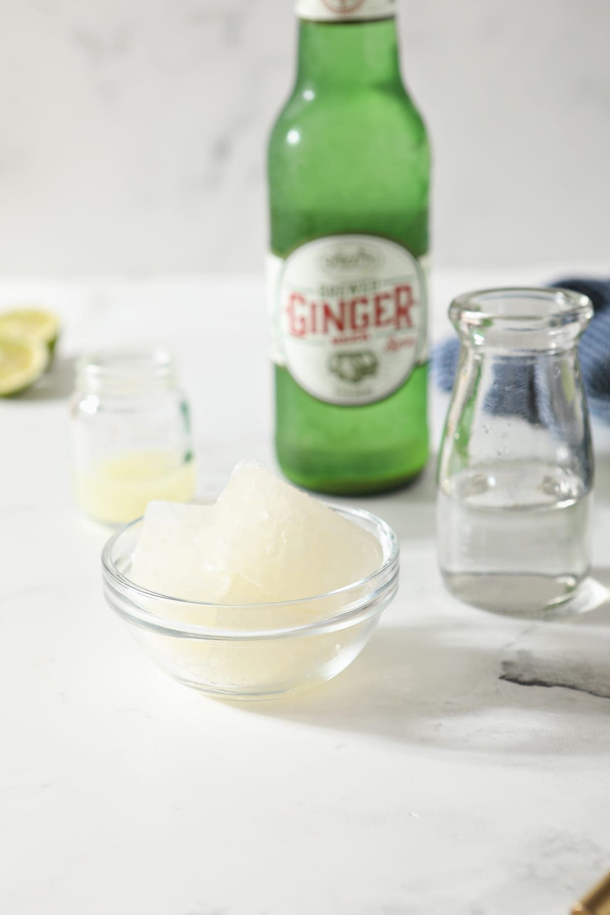 A bowl holds ginger beer ice cubes with bottles of lime juice, vodka and ginger beer