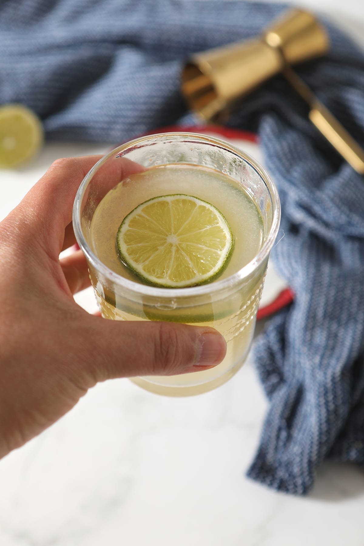 A person holds a glass of the slushy cocktail garnished with a round of lime