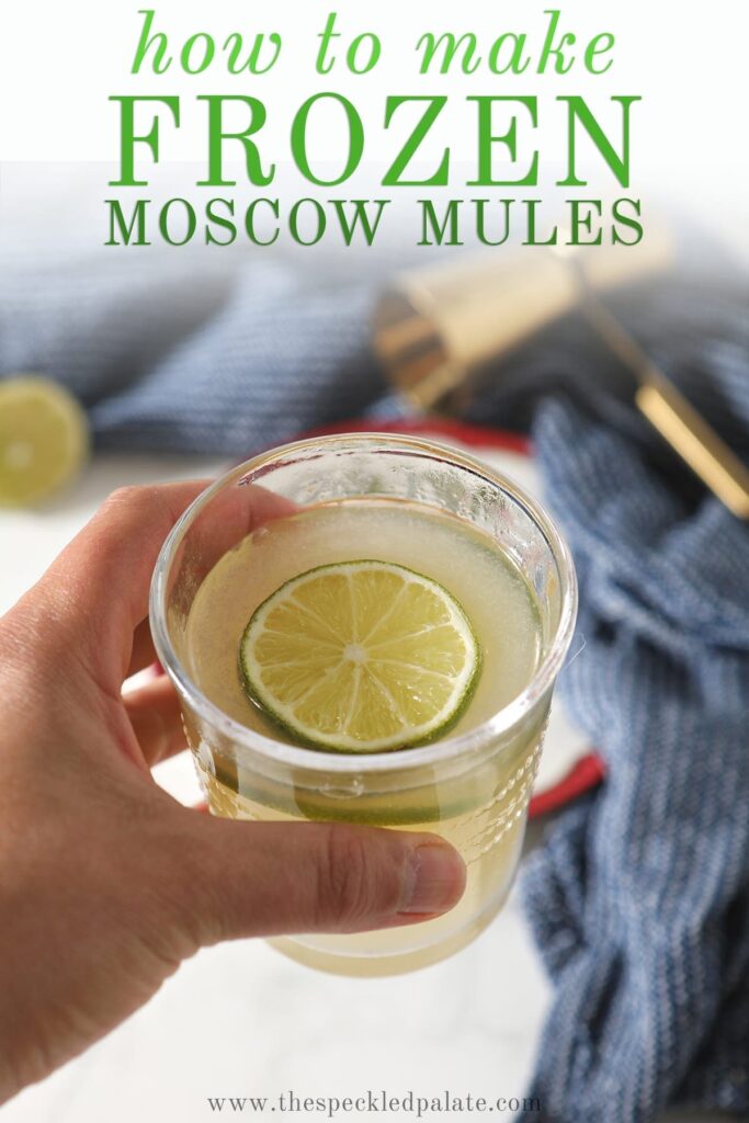 A person holds a glass of the slushy cocktail garnished with a round of lime with the text "How to Make Frozen Moscow Mules"