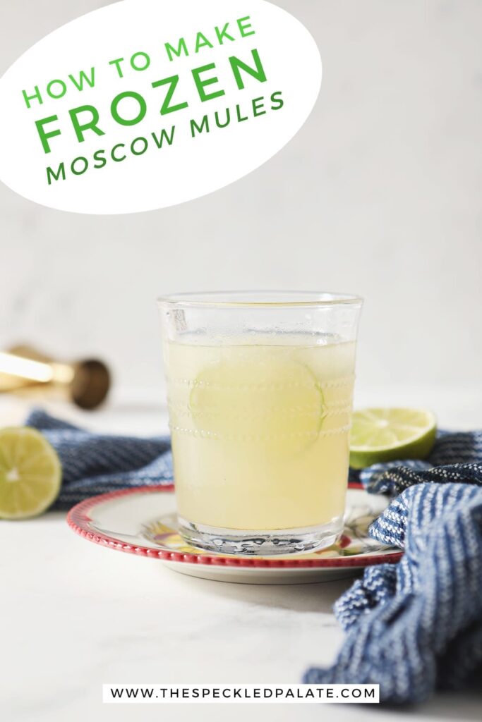 A glass of a Frozen Mule garnished with a lime round sits on a red-rimmed plate by a blue towel on marble with the text "How to make Frozen Moscow Mules"