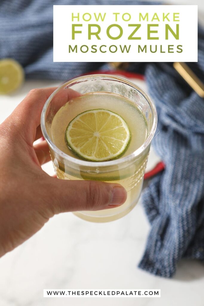 A person holds a glass of the slushy cocktail garnished with a round of lime with the text "How to Make Frozen Moscow Mules"