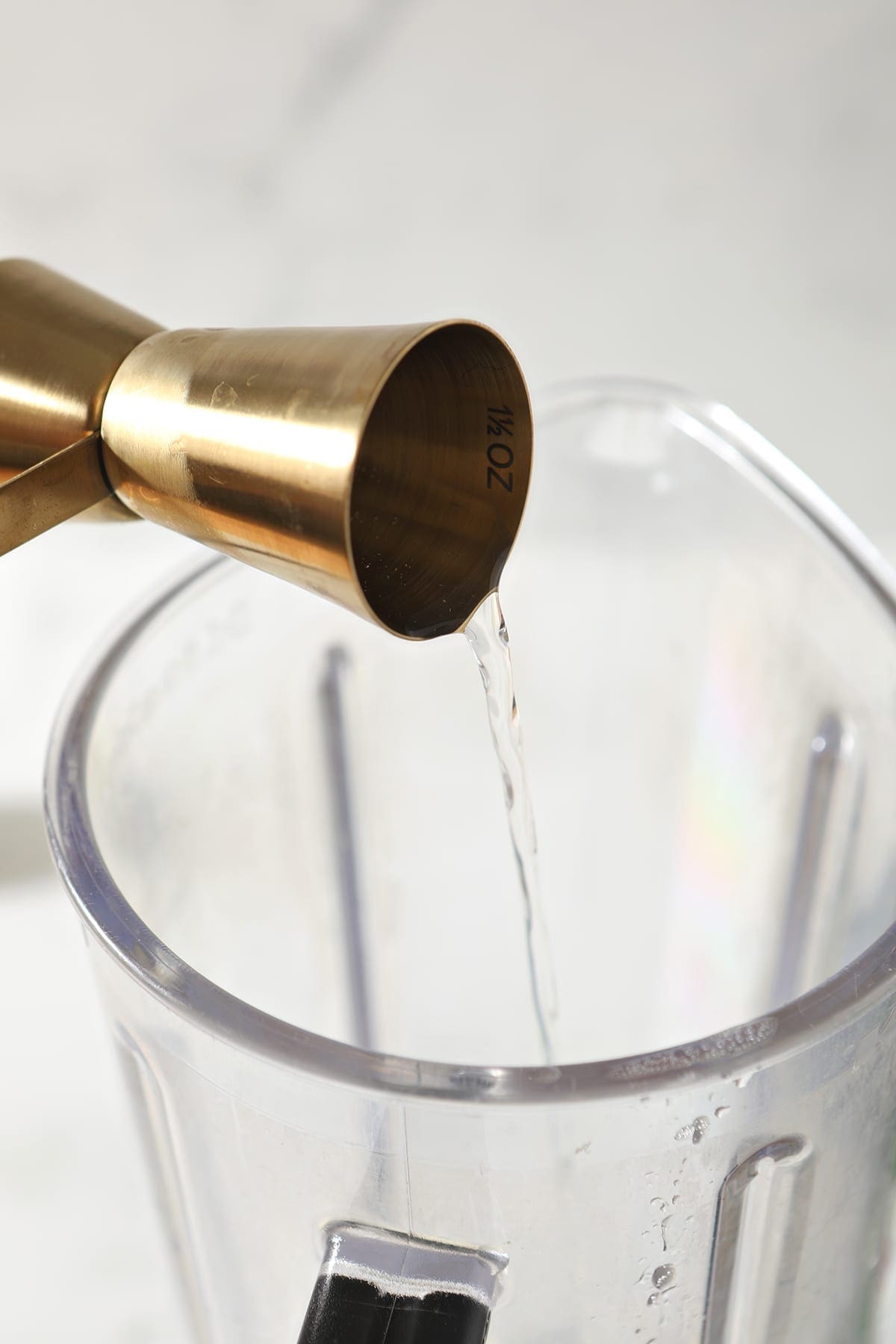 A gold jigger pours a liquid into a blender