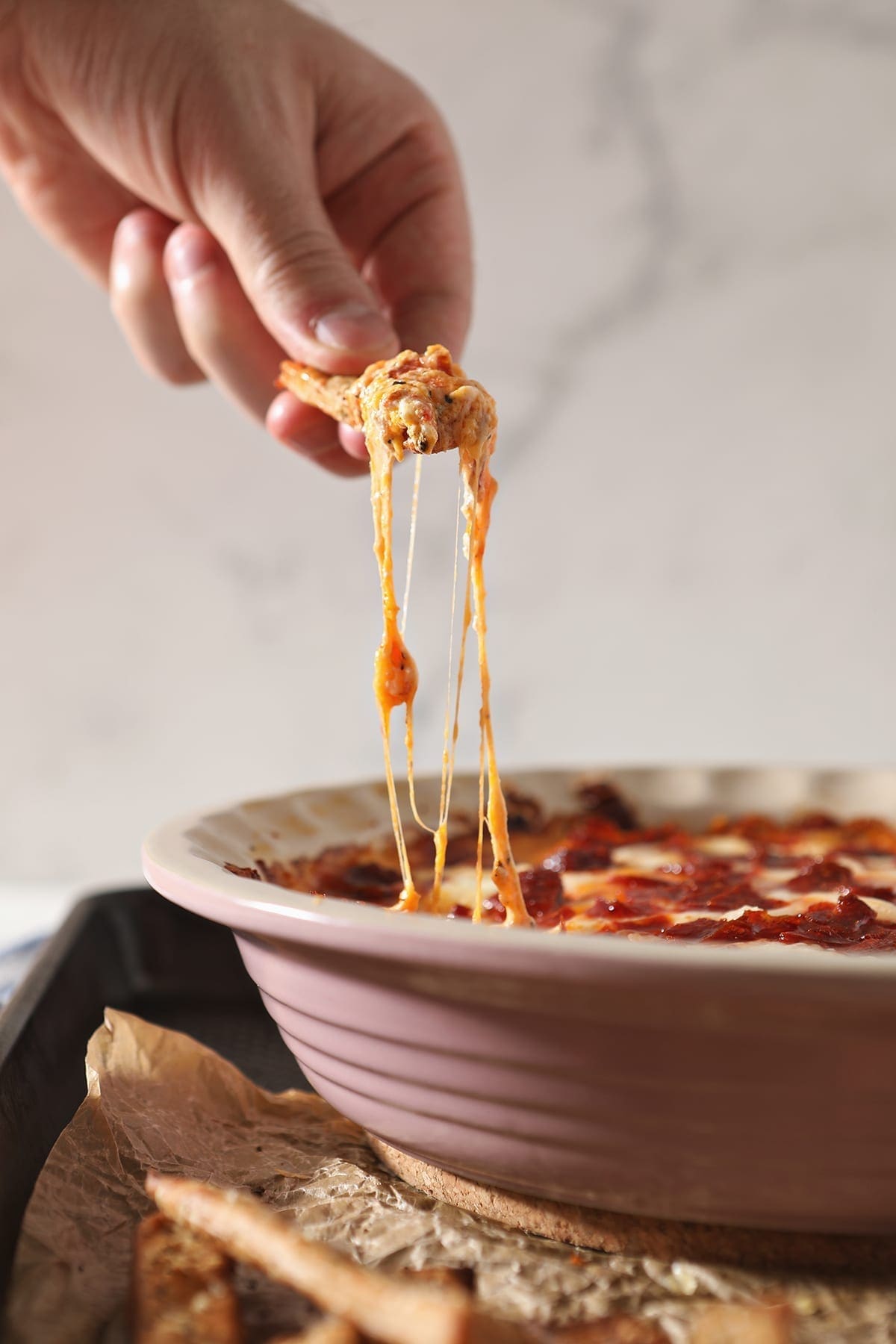 A breadstick lifts cheesy Pepperoni Dip out of a pie plate