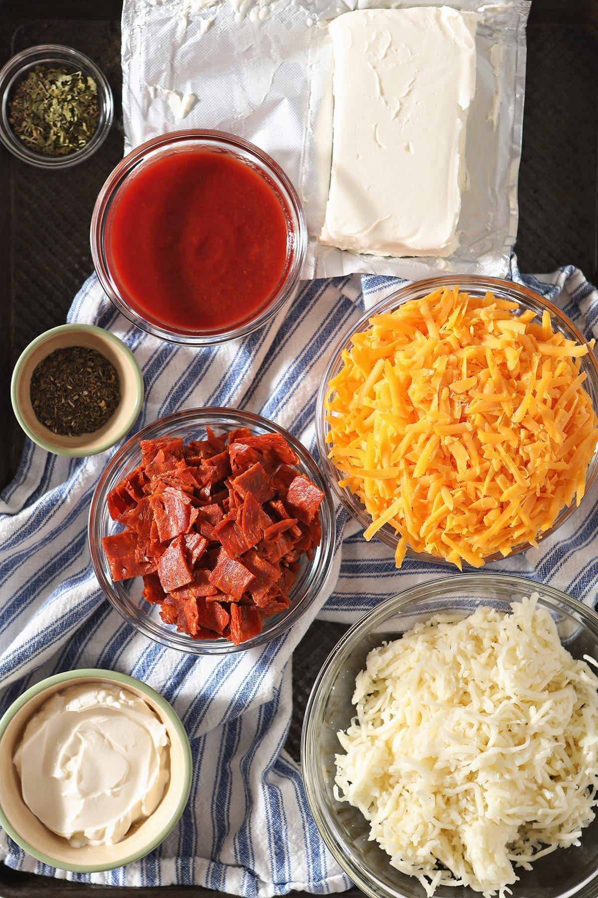 Ingredients for dip sit on a blue and white striped towel in a baking sheet