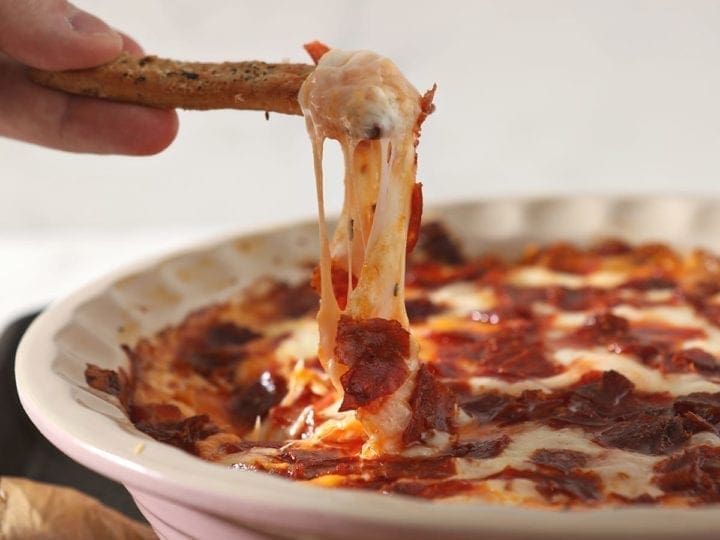 A breadstick lifts cheesy Pepperoni Dip out of a pie plate