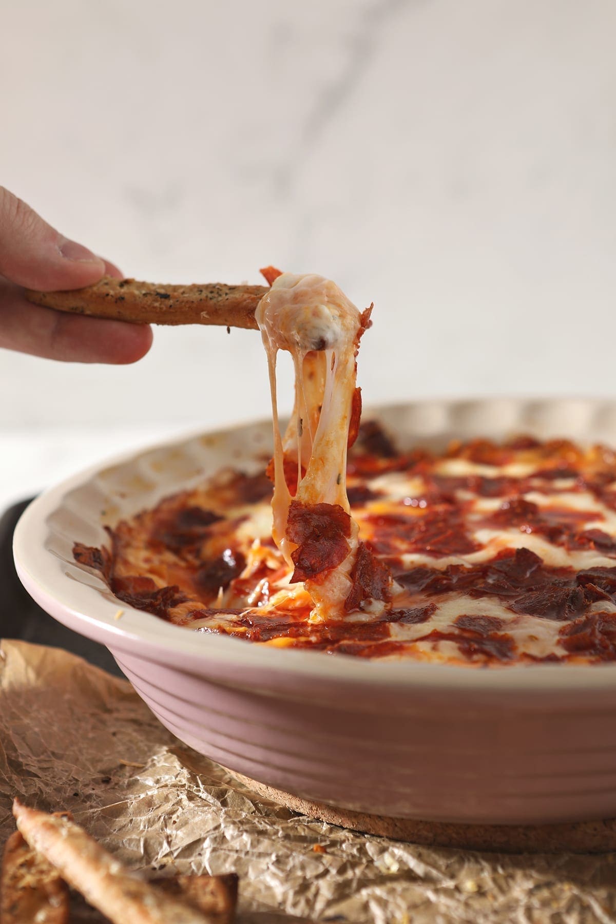 A breadstick lifts cheesy Pepperoni Dip out of a pie plate