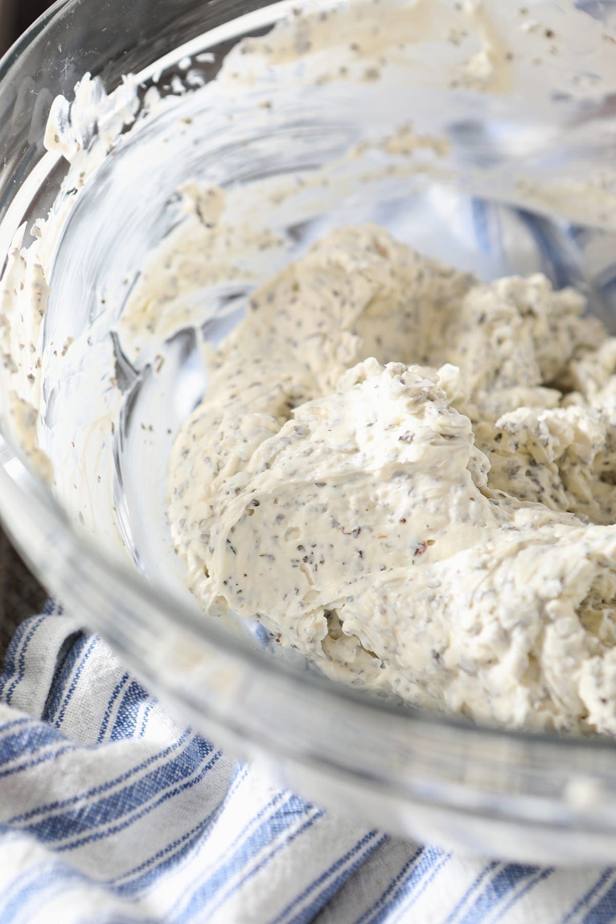 Close up of a creamy, herb-studded cheese mixture in a glass bowl