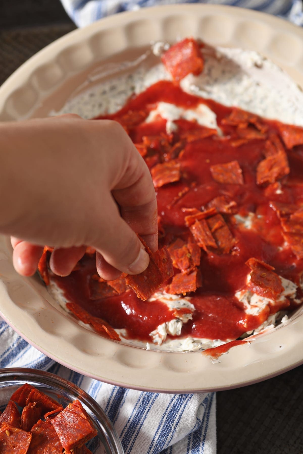 A woman places pepperoni pieces on top of pizza sauce in a pie plate