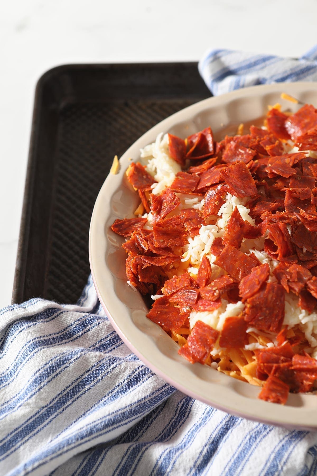 Chopped pepperoni sits on top of cheeses in a pie plate