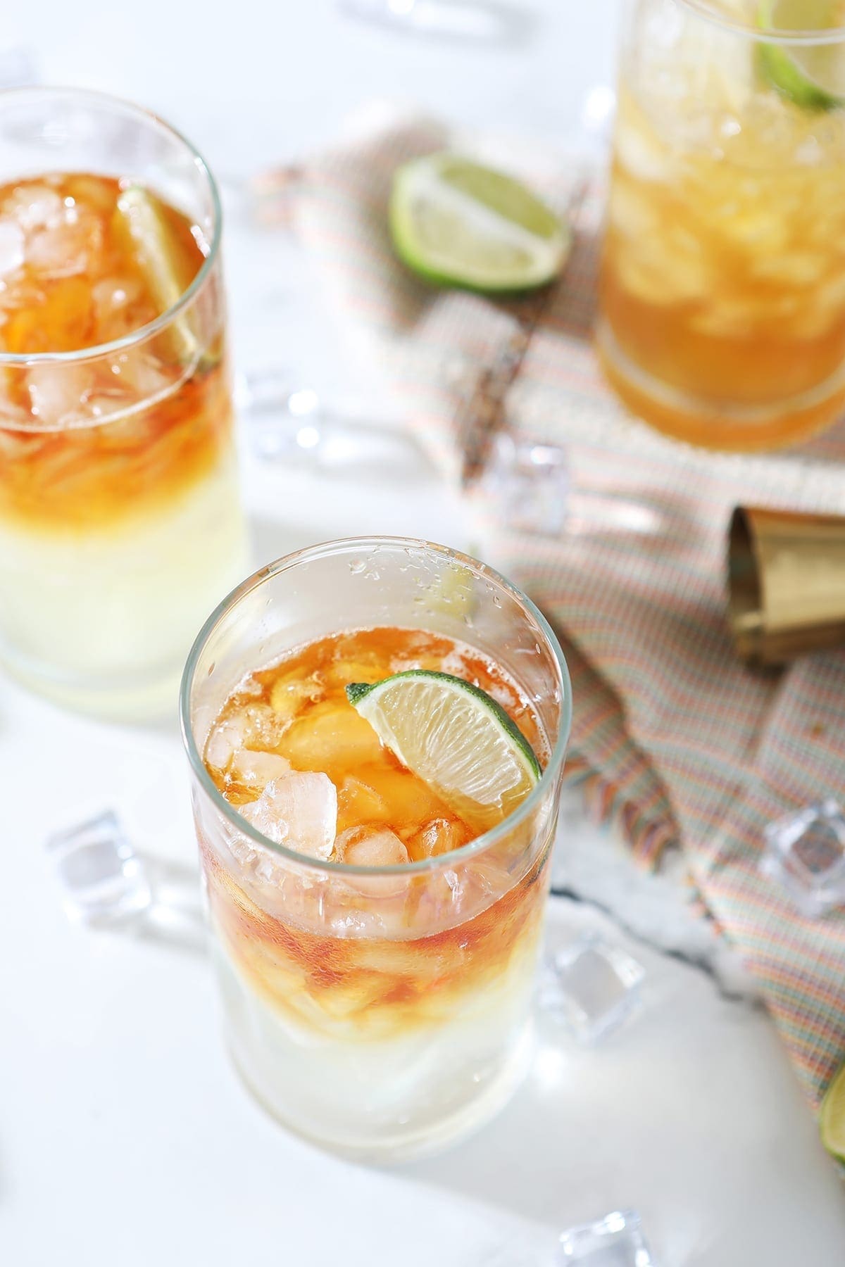 Three Rum Moscow Mules garnished with lime on marble with ice, lime wedges and a gold jigger