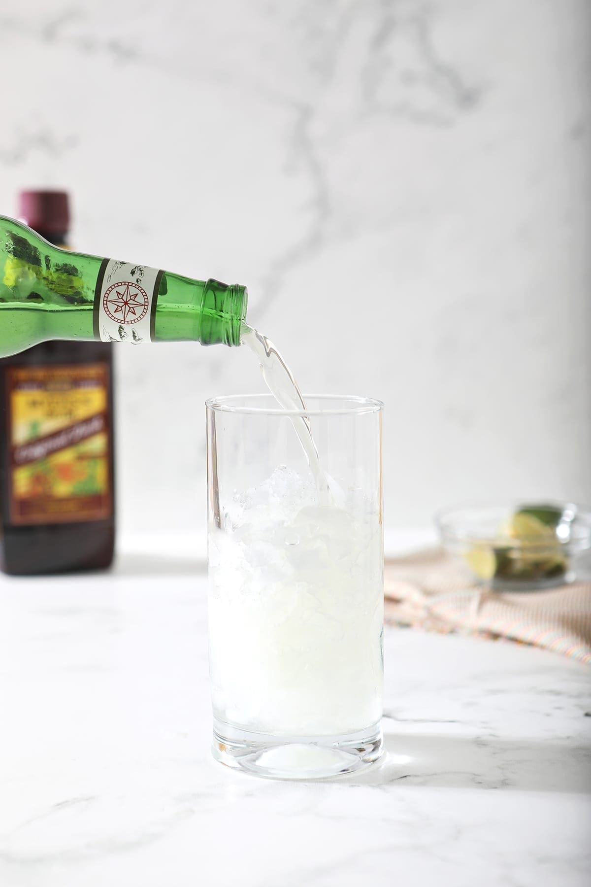 Ginger beer is poured into a highball glass with crushed ice cubes on marble