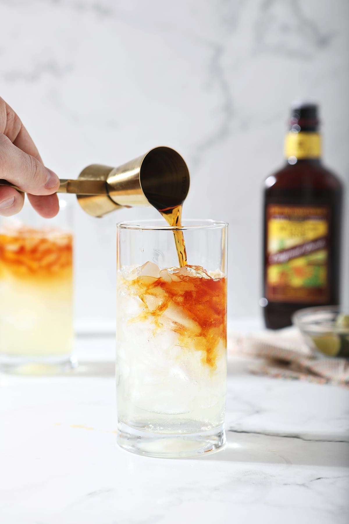 A jigger pours dark rum into a glass with ginger beer