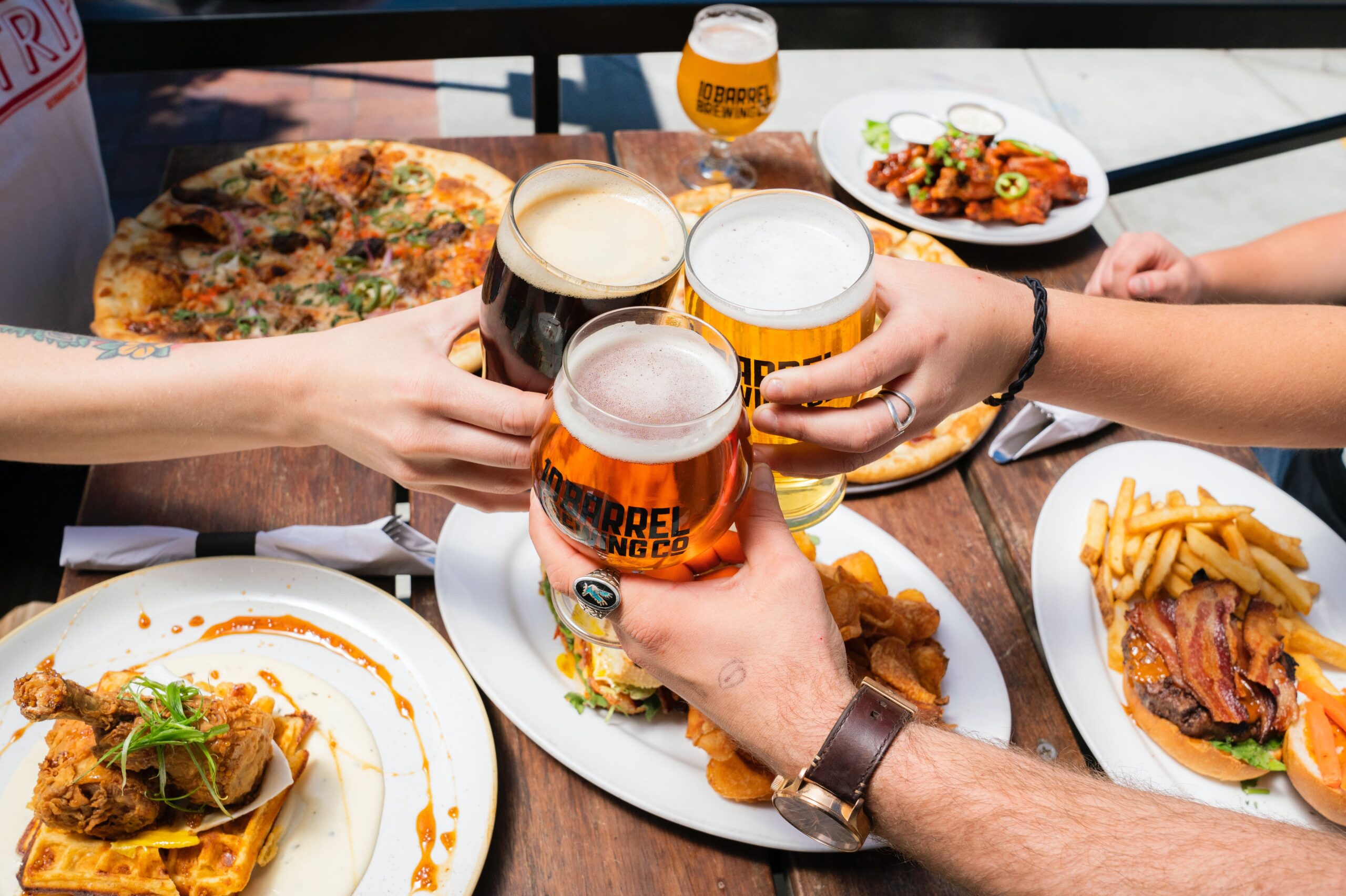 People at a table with food clink beer glasses together