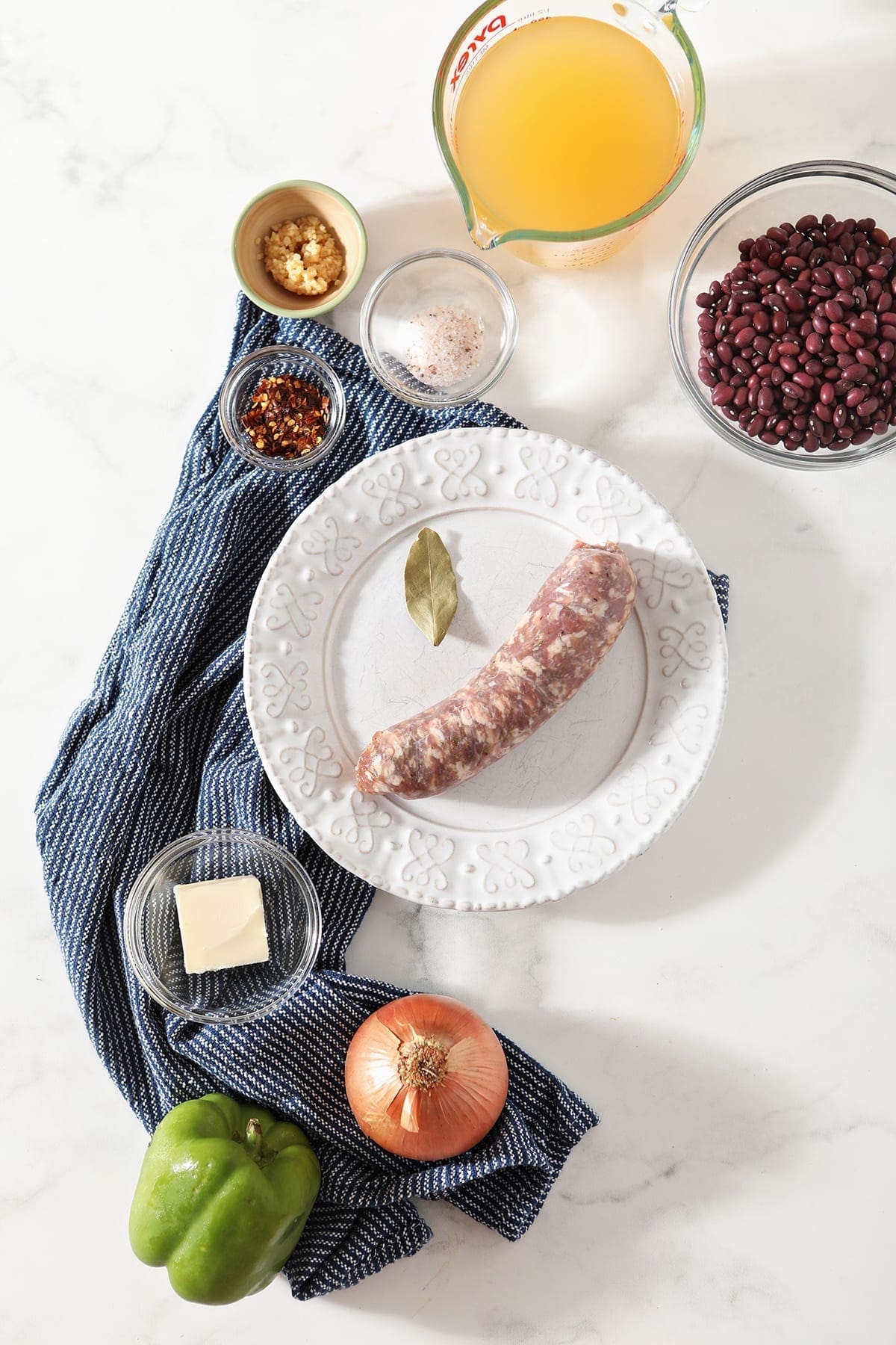 Ingredients for the recipe, including sausage, butter, onion, bell pepper, red beans and more, on marble