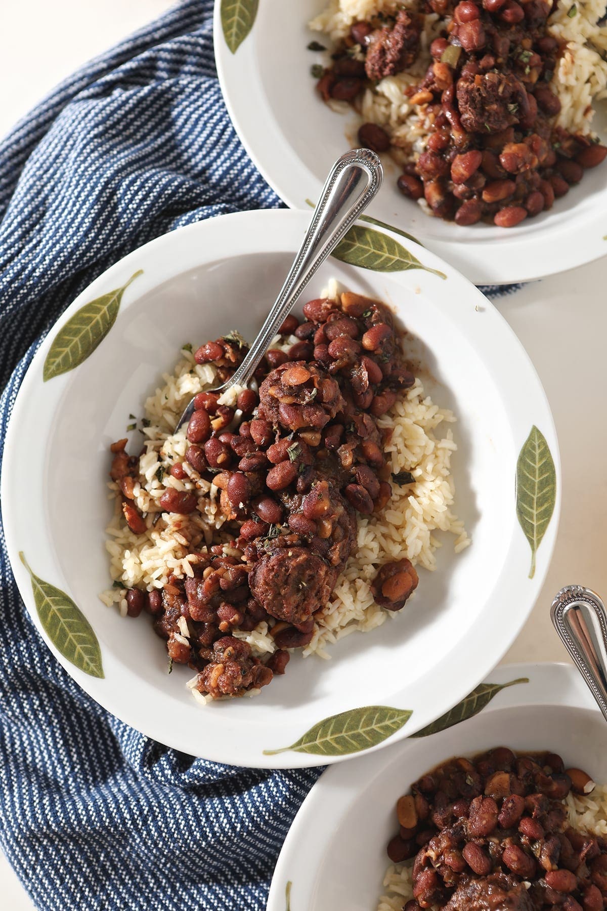 Overhead of three white bowls holding Red Beans and Rice on a blue striped towel