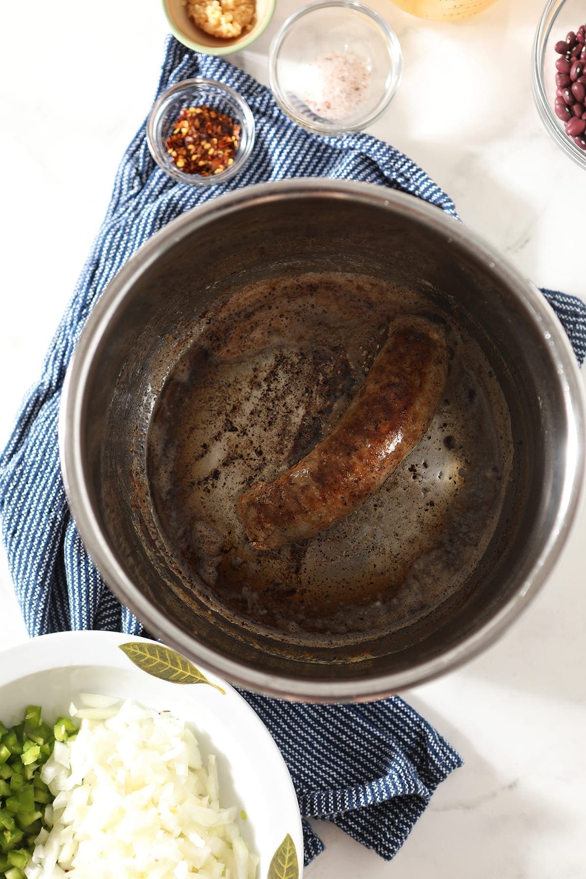 A cooked sausage in butter in the Instant Pot, surrounded by other Red Beans and Rice ingredients