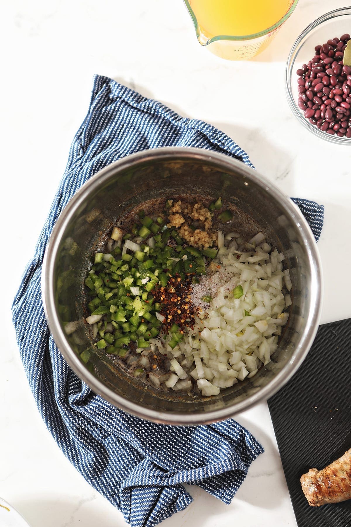 Chopped onions, bell pepper and garlic with seasonings in the pot of the Instant Pot on a blue towel on marble