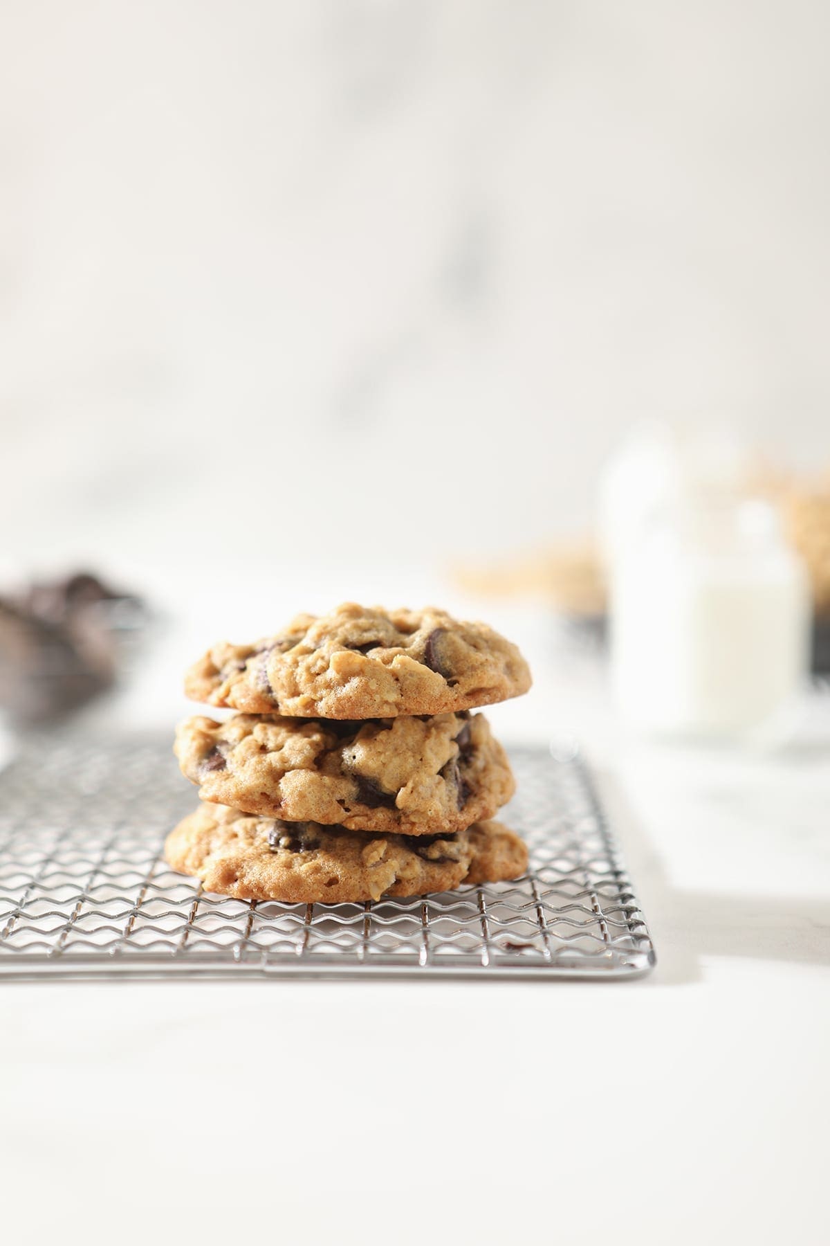 Three oatmeal chocolate chip cookies stacked on top of each other on a wire cooling rack