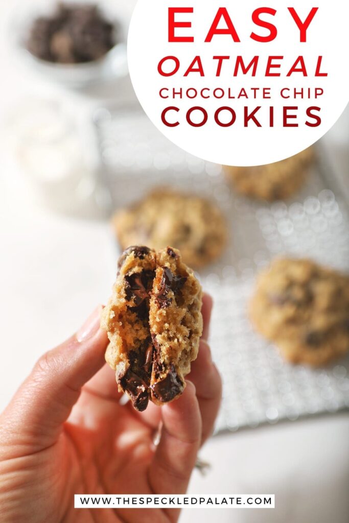 A woman holds a halved chocolate chip cookie above other cookies on a wire cooling rack with the text 'easy oatmeal chocolate chip cookies'