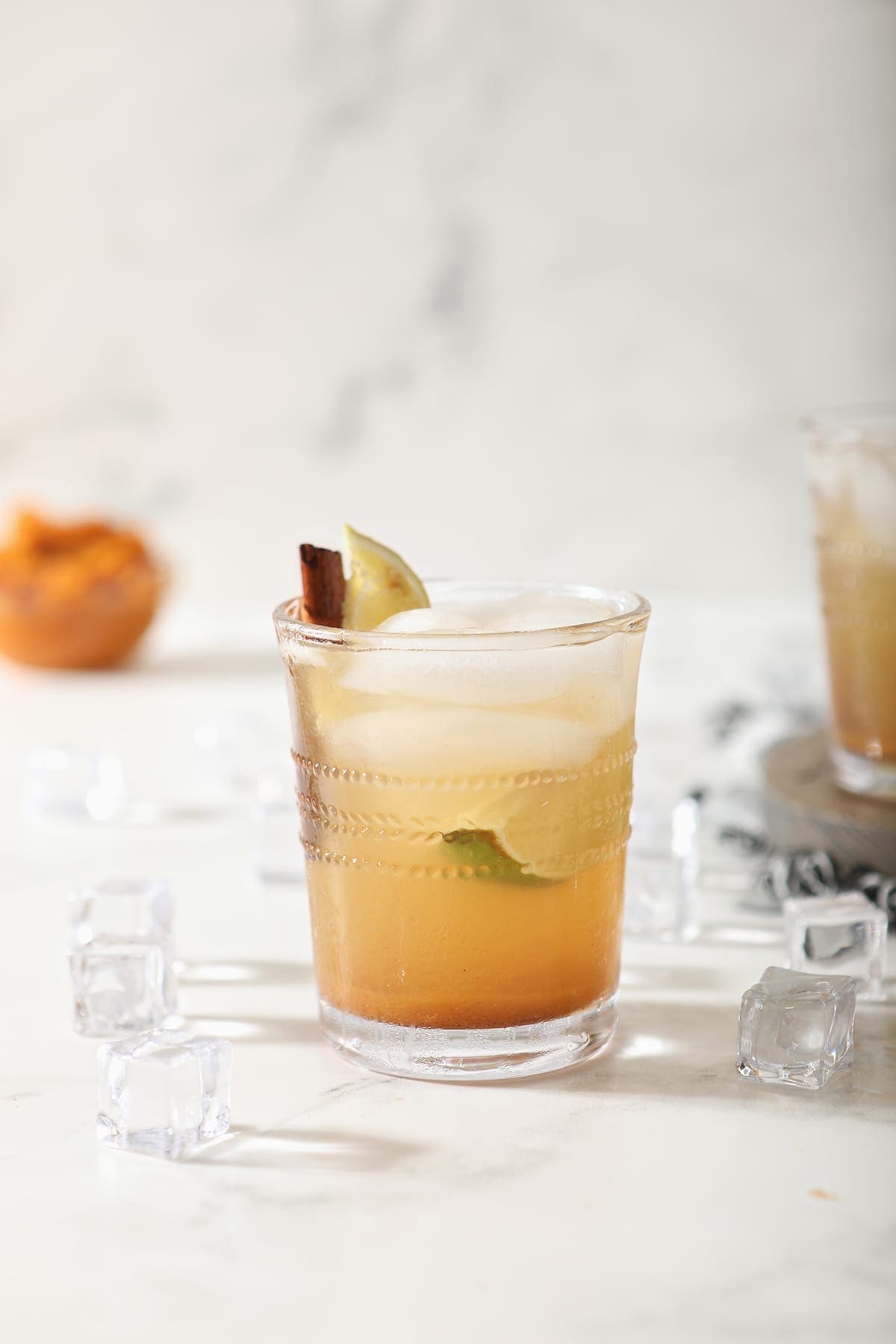 A singular glass of Pumpkin Spice Mule on marble with a bowl of pumpkin puree behind it