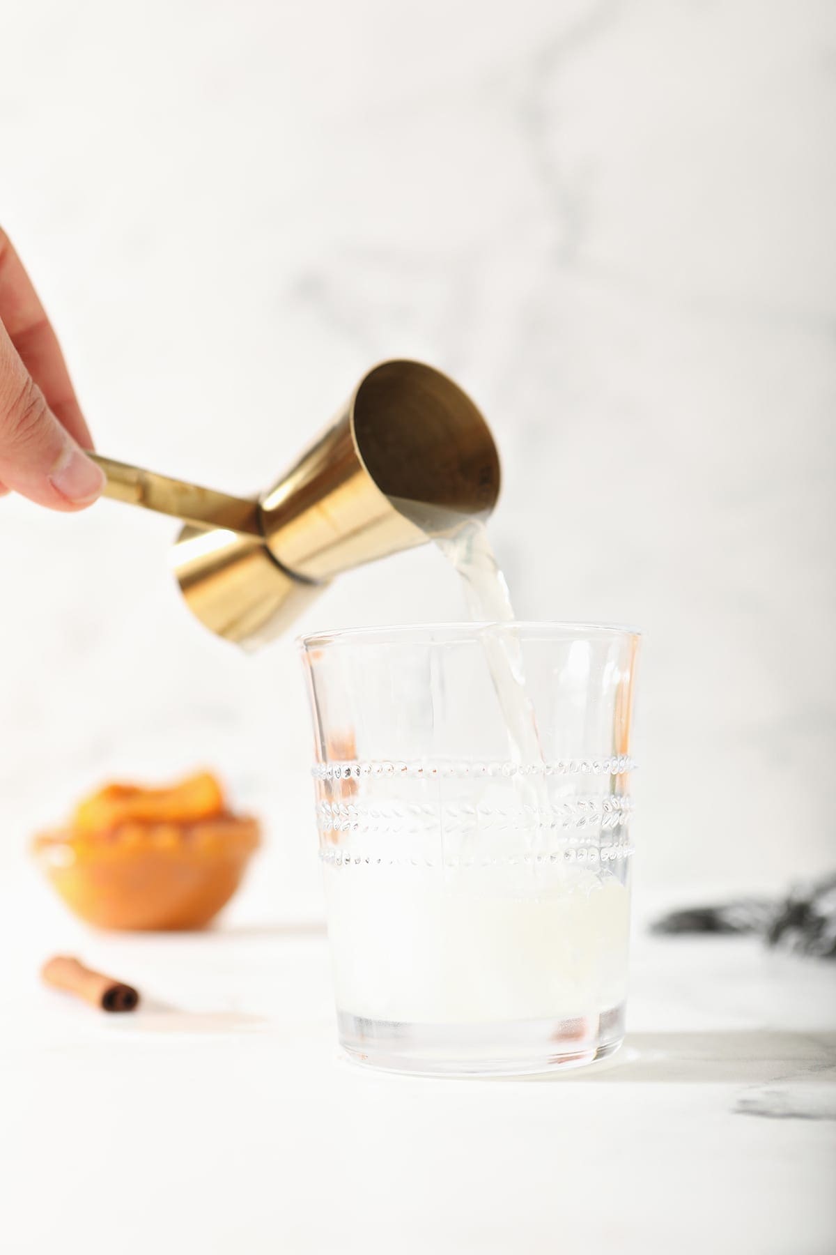 Ginger beer pours into a glass from a gold jigger