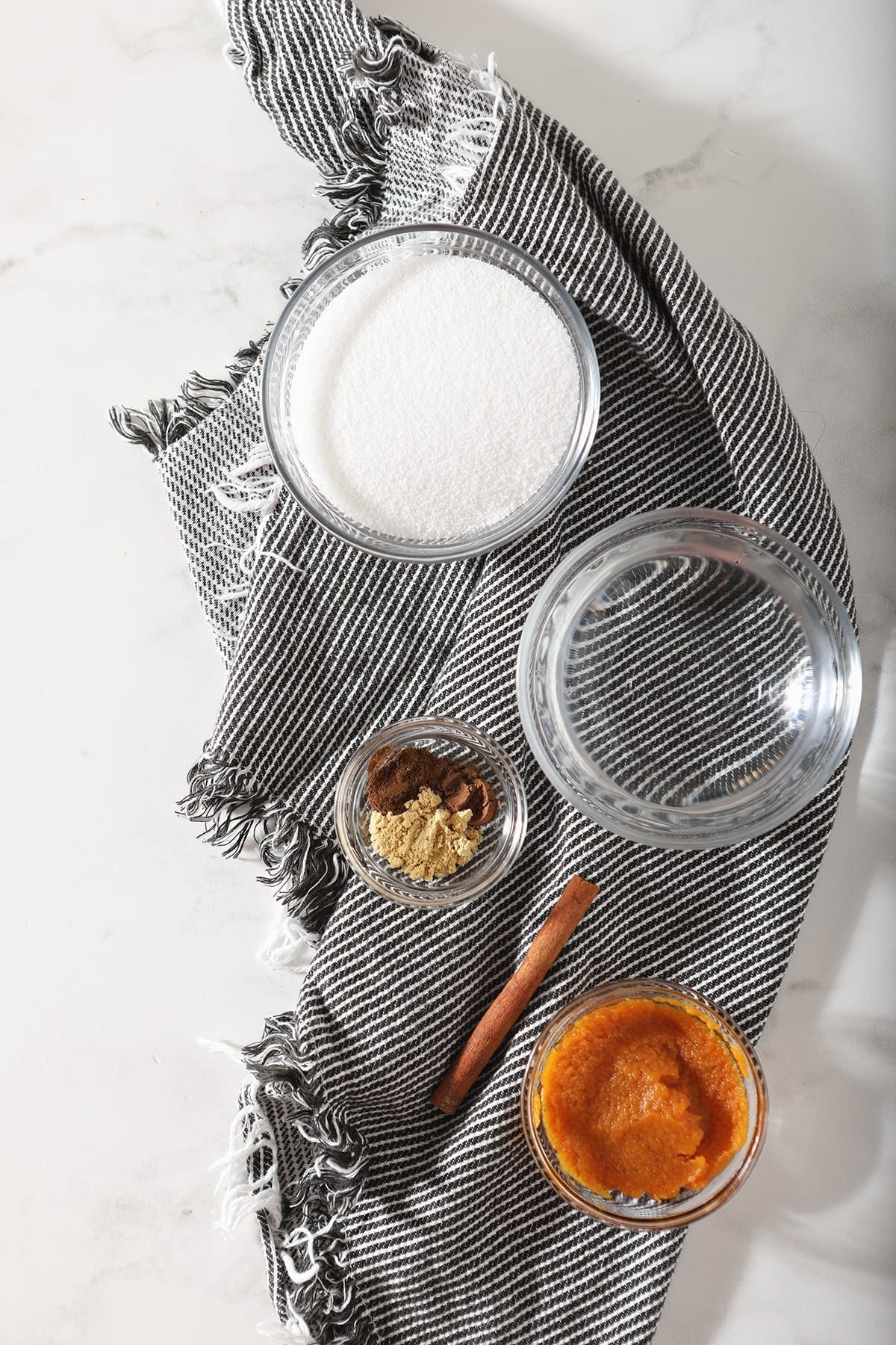 Granulated sugar, water, pumpkin pure and spices sit on a gray striped towel on marble