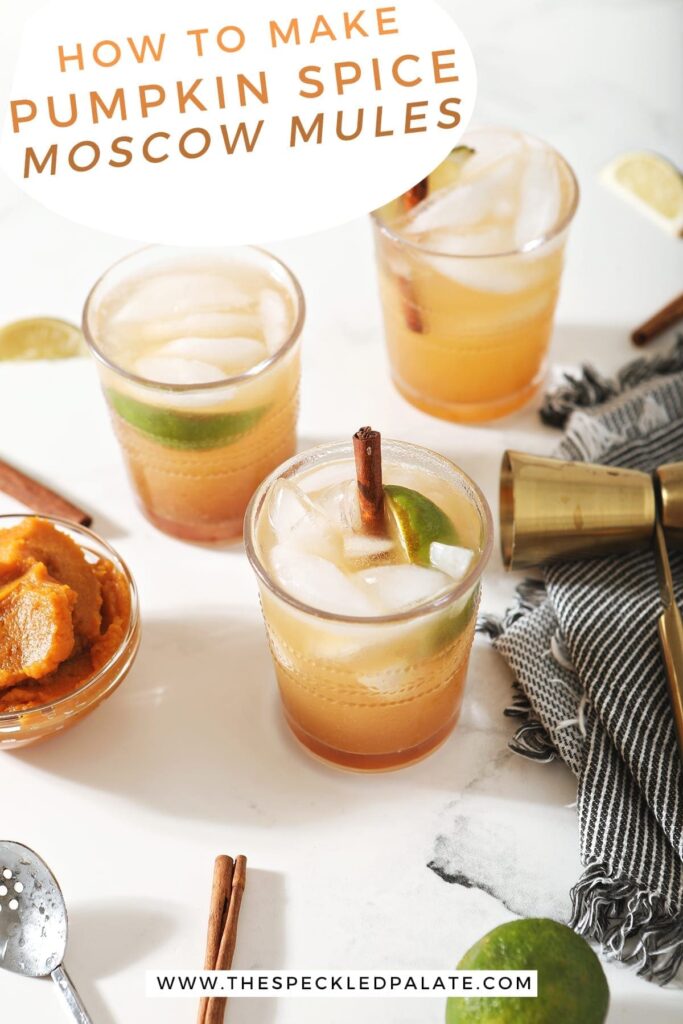 Three Pumpkin Mules, garnished with cinnamon sticks and lime wedges, surrounded by limes, pumpkin and a jigger on marble with the text 'how to make pumpkin spice moscow mules'