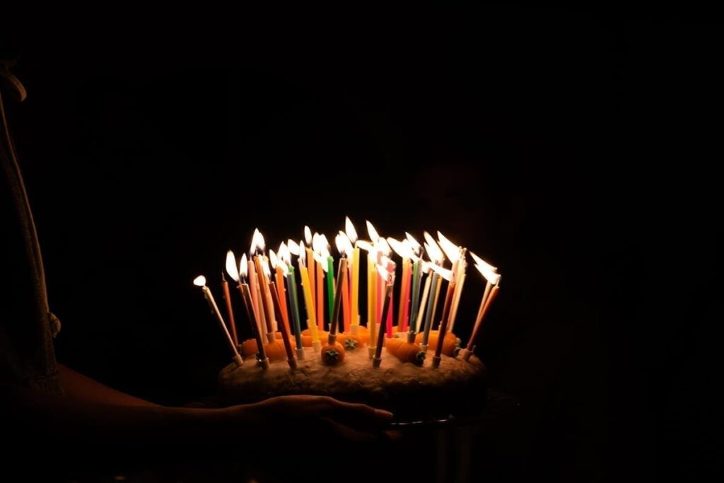 A person holds a birthday cake with lit candles in darkness