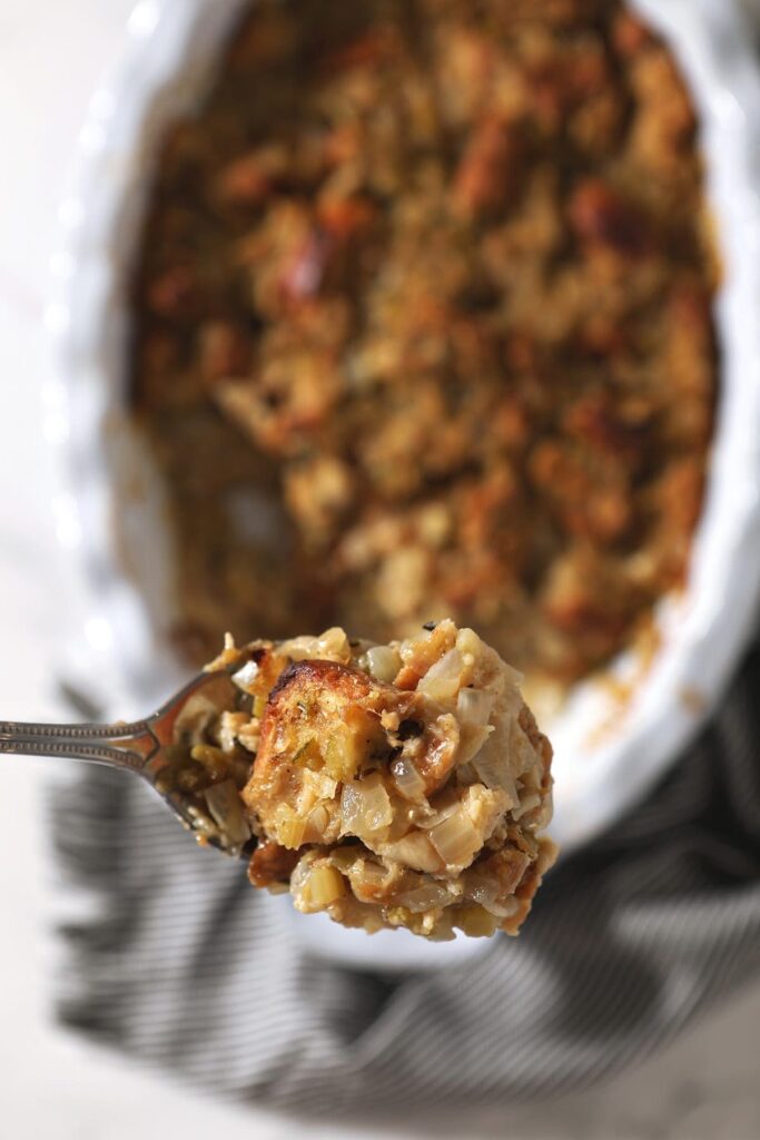 A large spoon holds a scoop of bread stuffing above a casserole dish